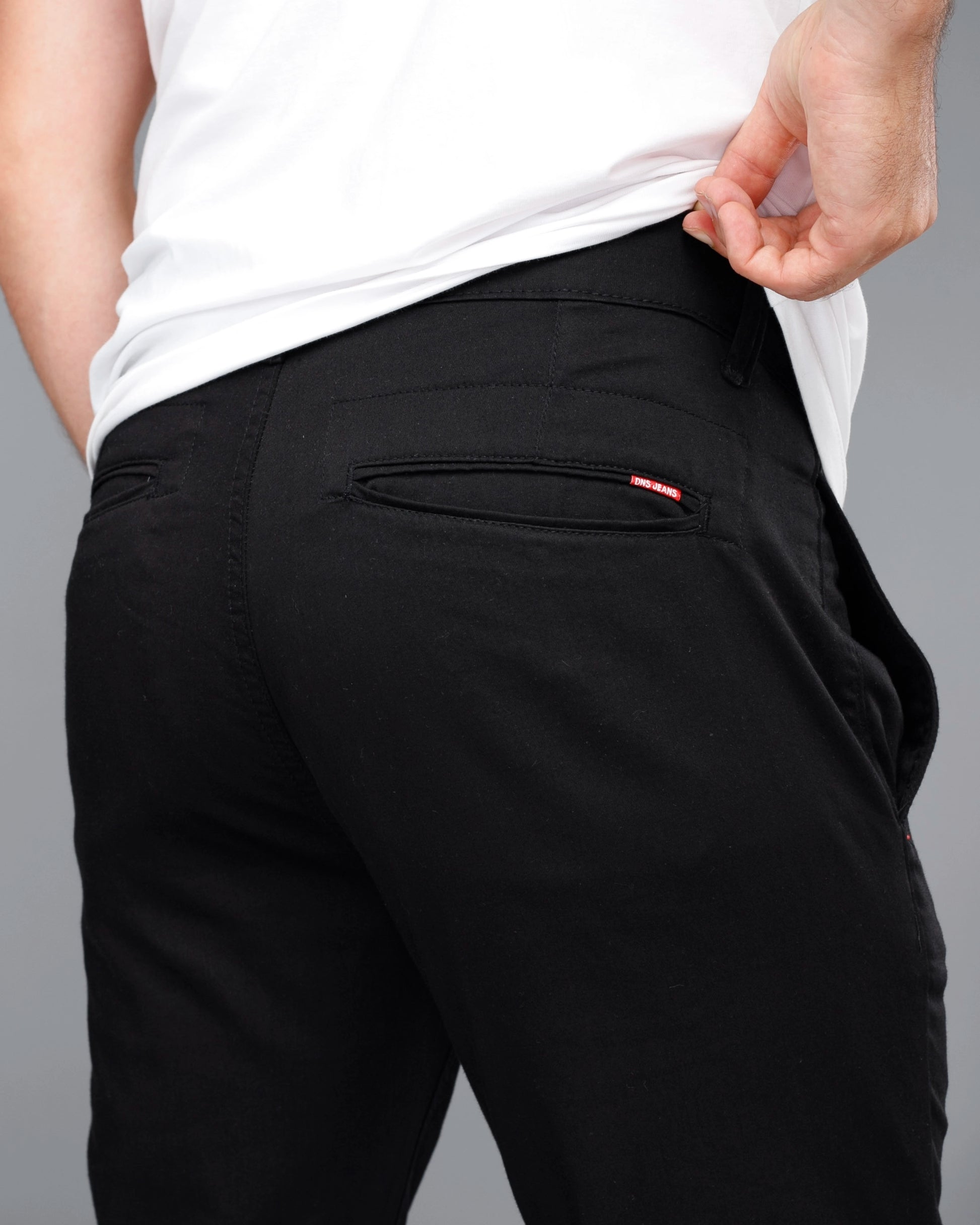 Person wearing black pants with a pocket detail on a gray background