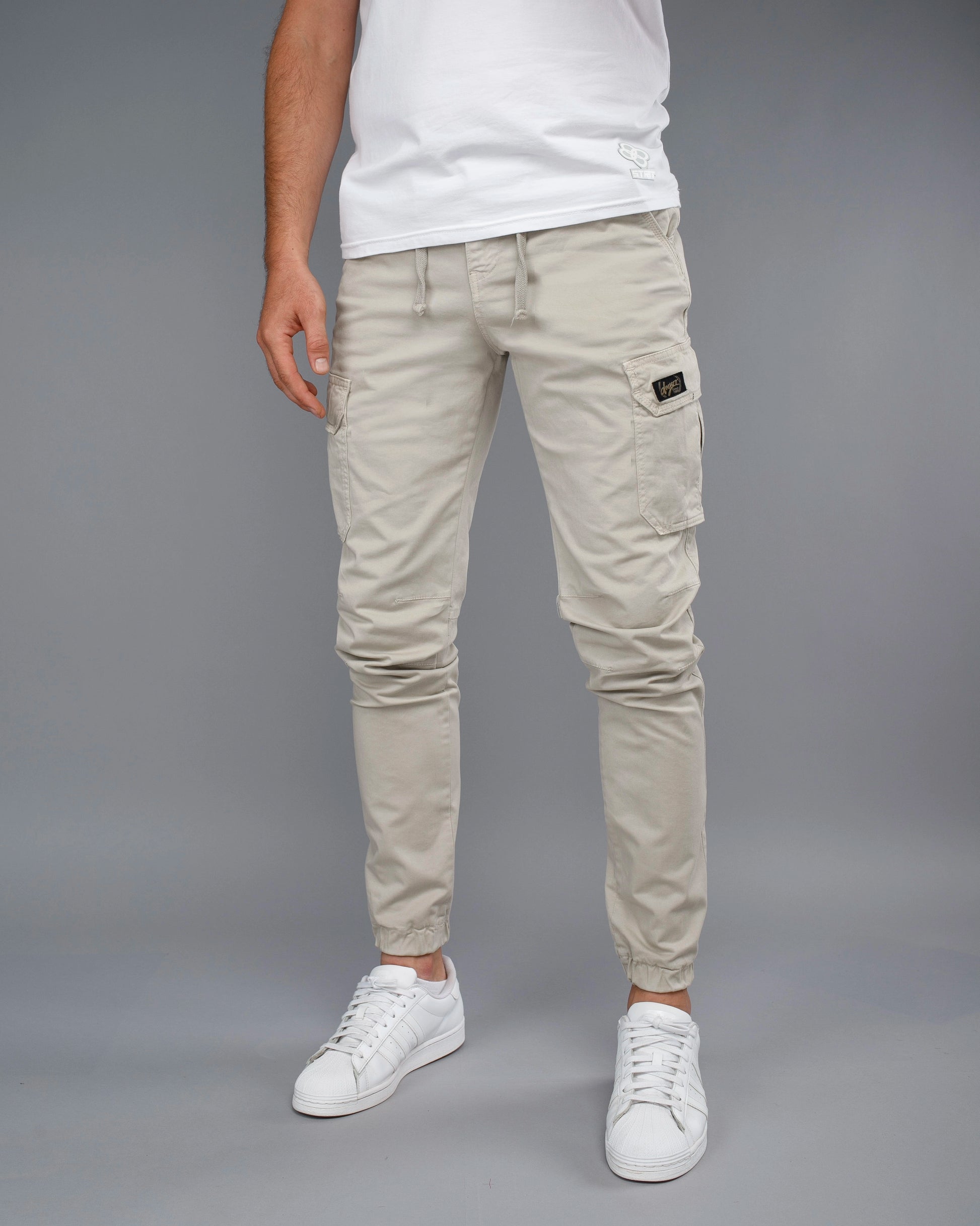 Person wearing light gray cargo pants and white sneakers on a gray background