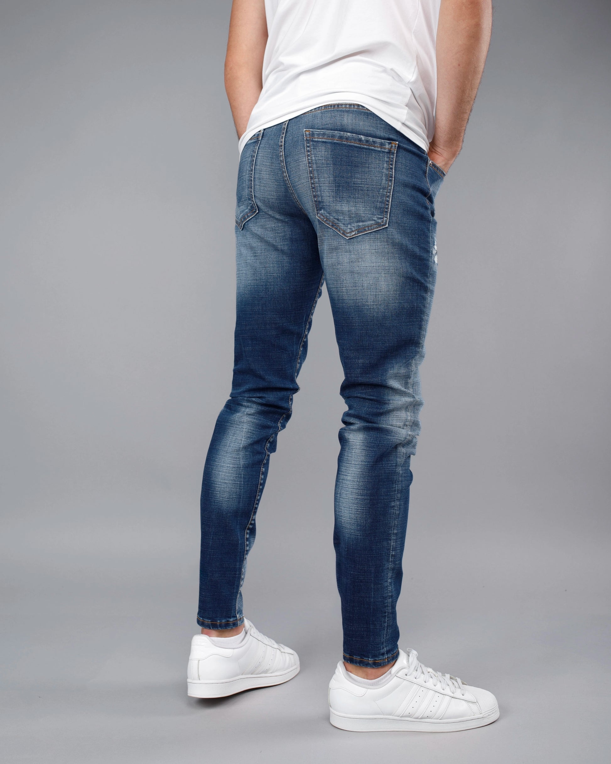 Person wearing blue jeans and white sneakers on a gray background