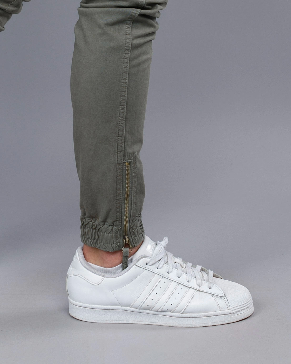 White Adidas Superstar sneakers worn with green pants on a gray background