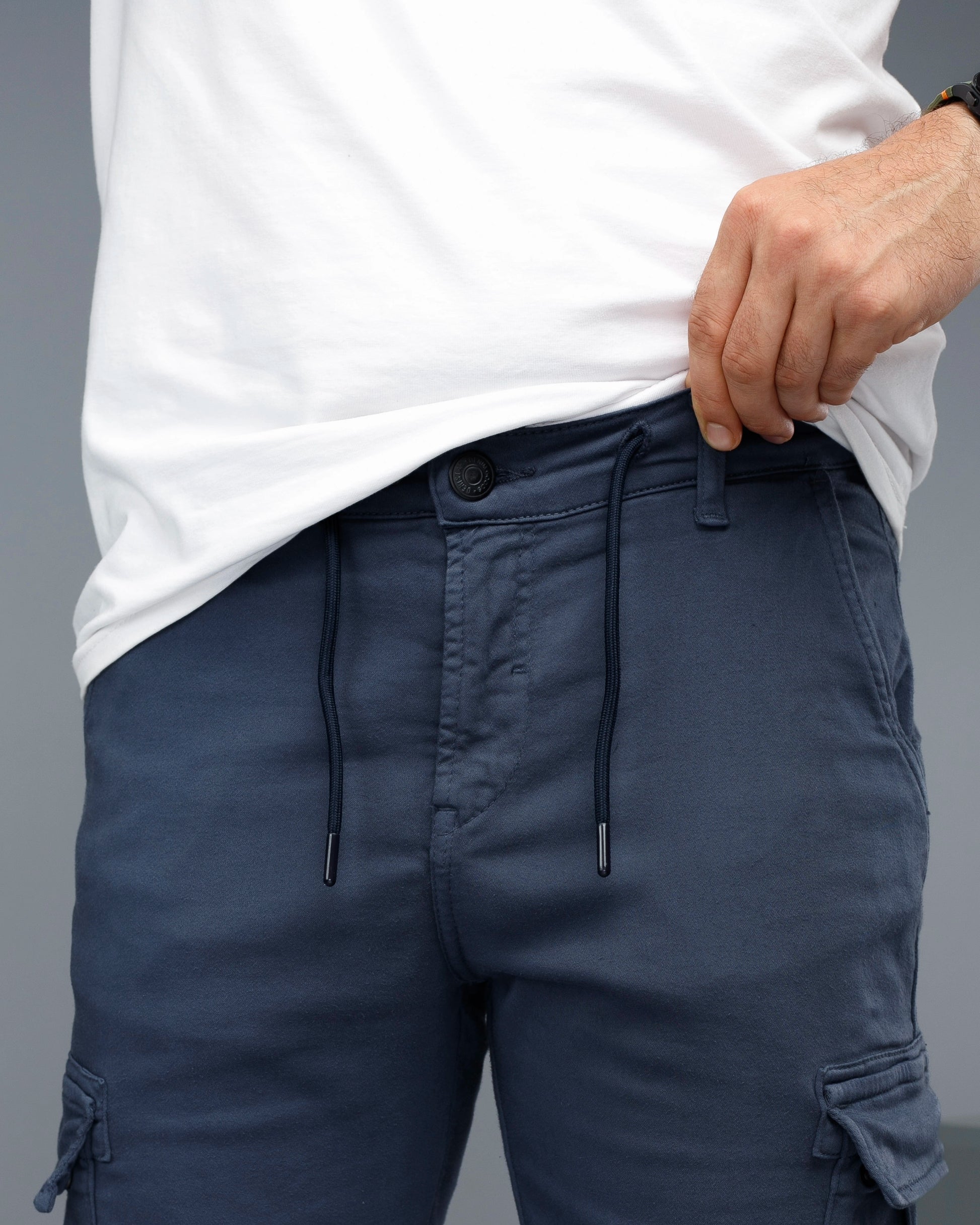 Person wearing navy cargo shorts with a white shirt on a gray background