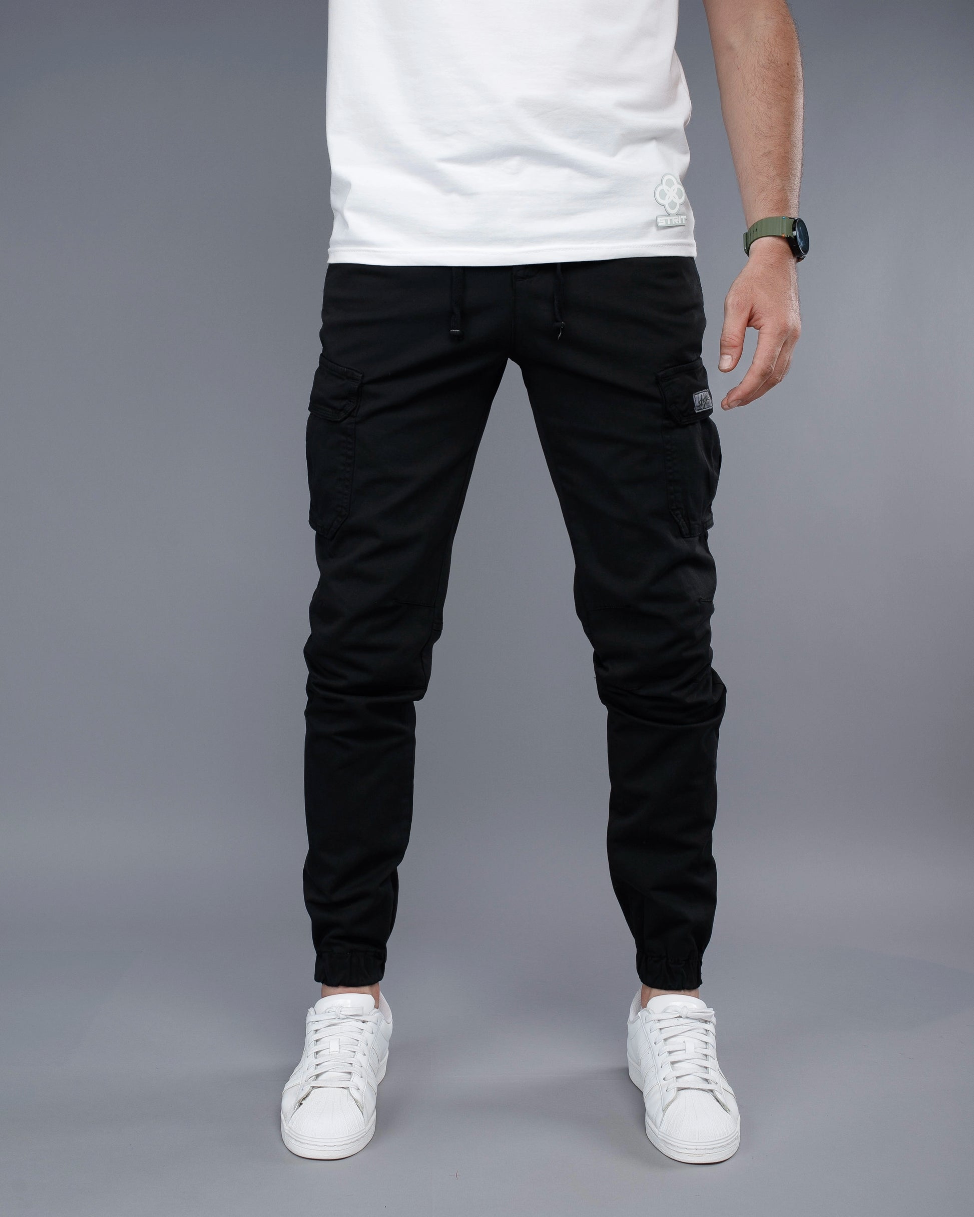Person wearing black jogger pants and white sneakers on a gray background