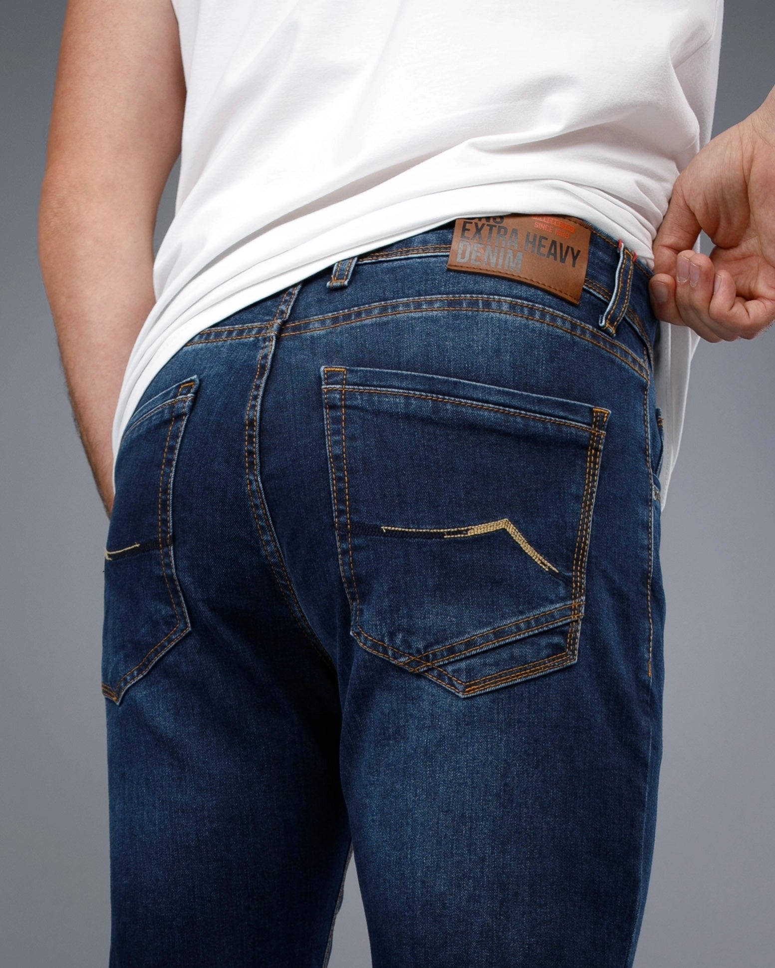 Person wearing blue jeans with a visible brand label on a gray background