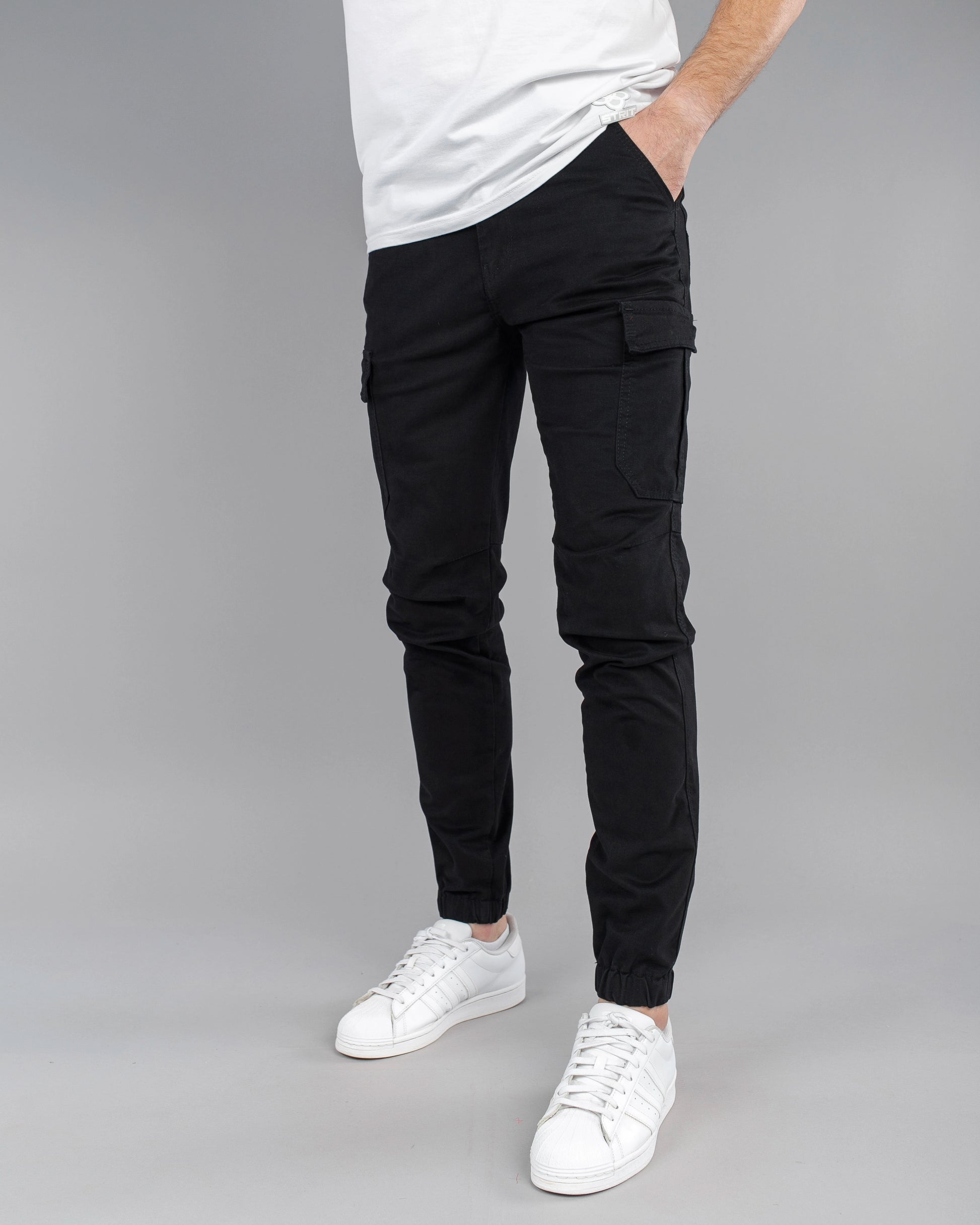 Person wearing black cargo pants and white sneakers on a gray background