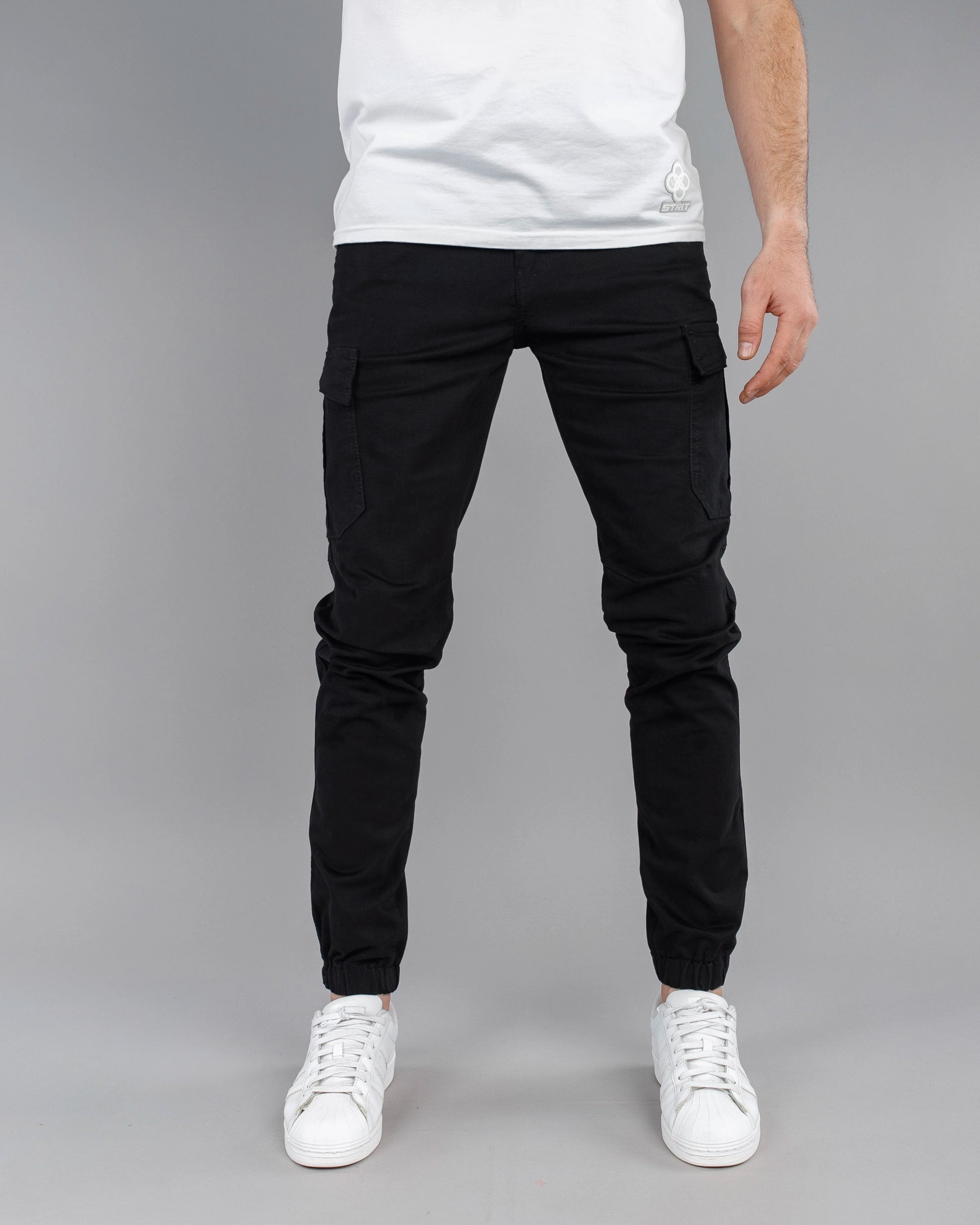 Person wearing black cargo jogger pants and white sneakers on a gray background