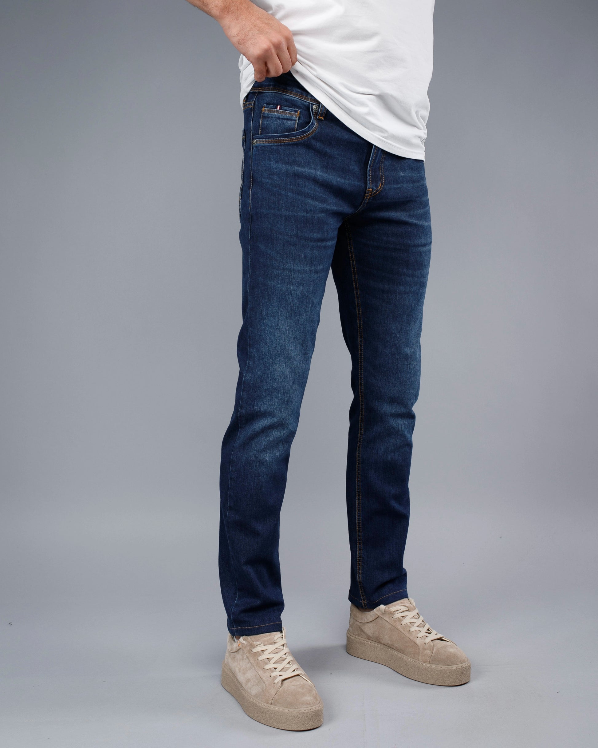 Person wearing blue jeans and beige sneakers on a gray background