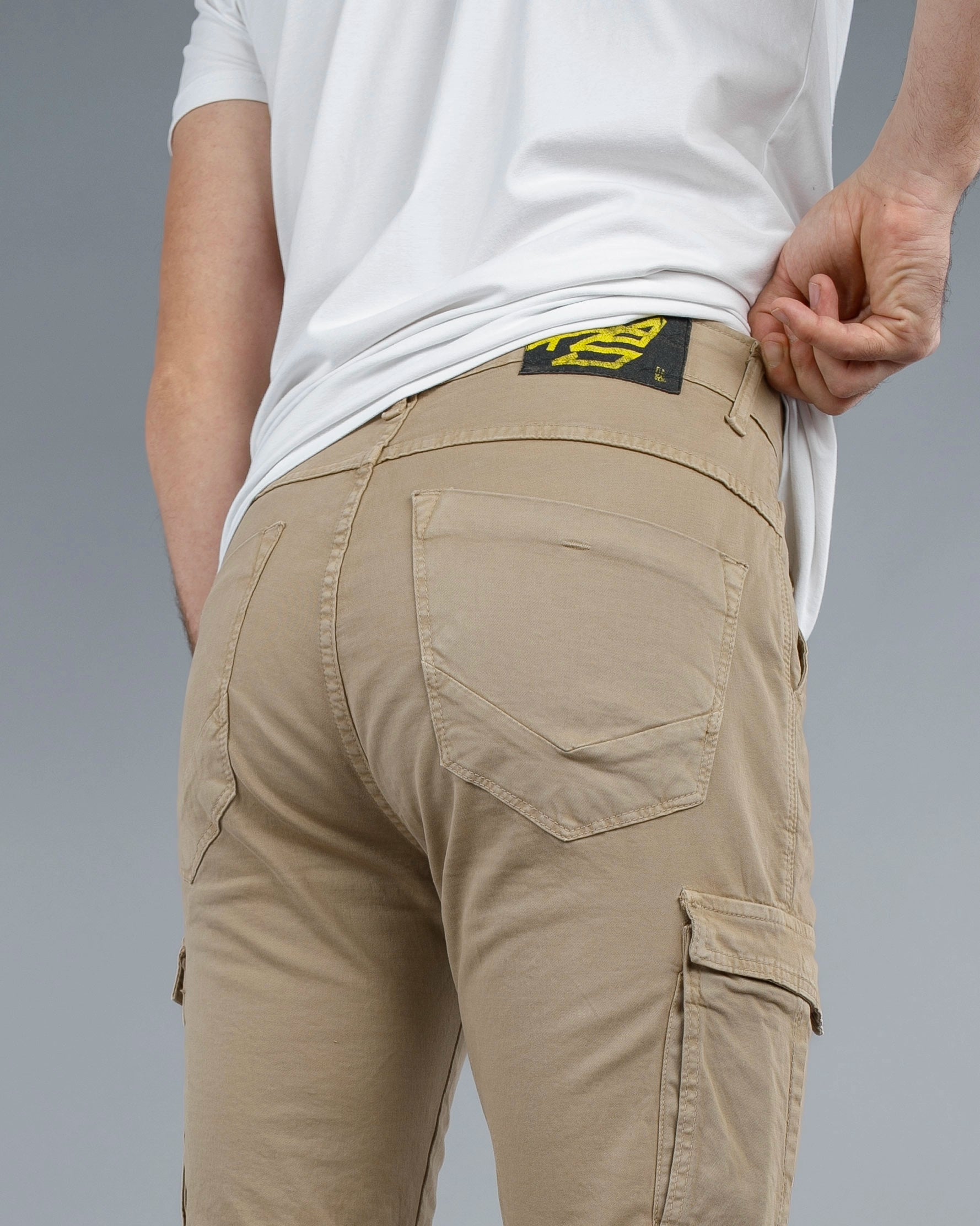 Person wearing beige cargo pants with a white shirt on a gray background