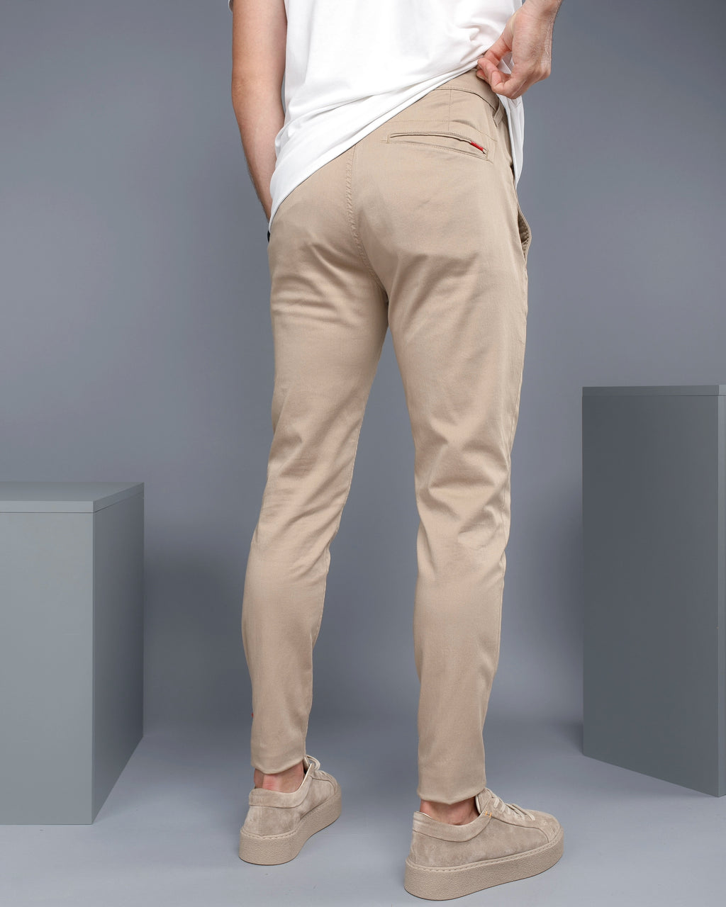 Person wearing beige pants and white shirt against a gray background