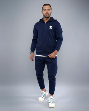 Man wearing a navy blue tracksuit with a logo on a gray background