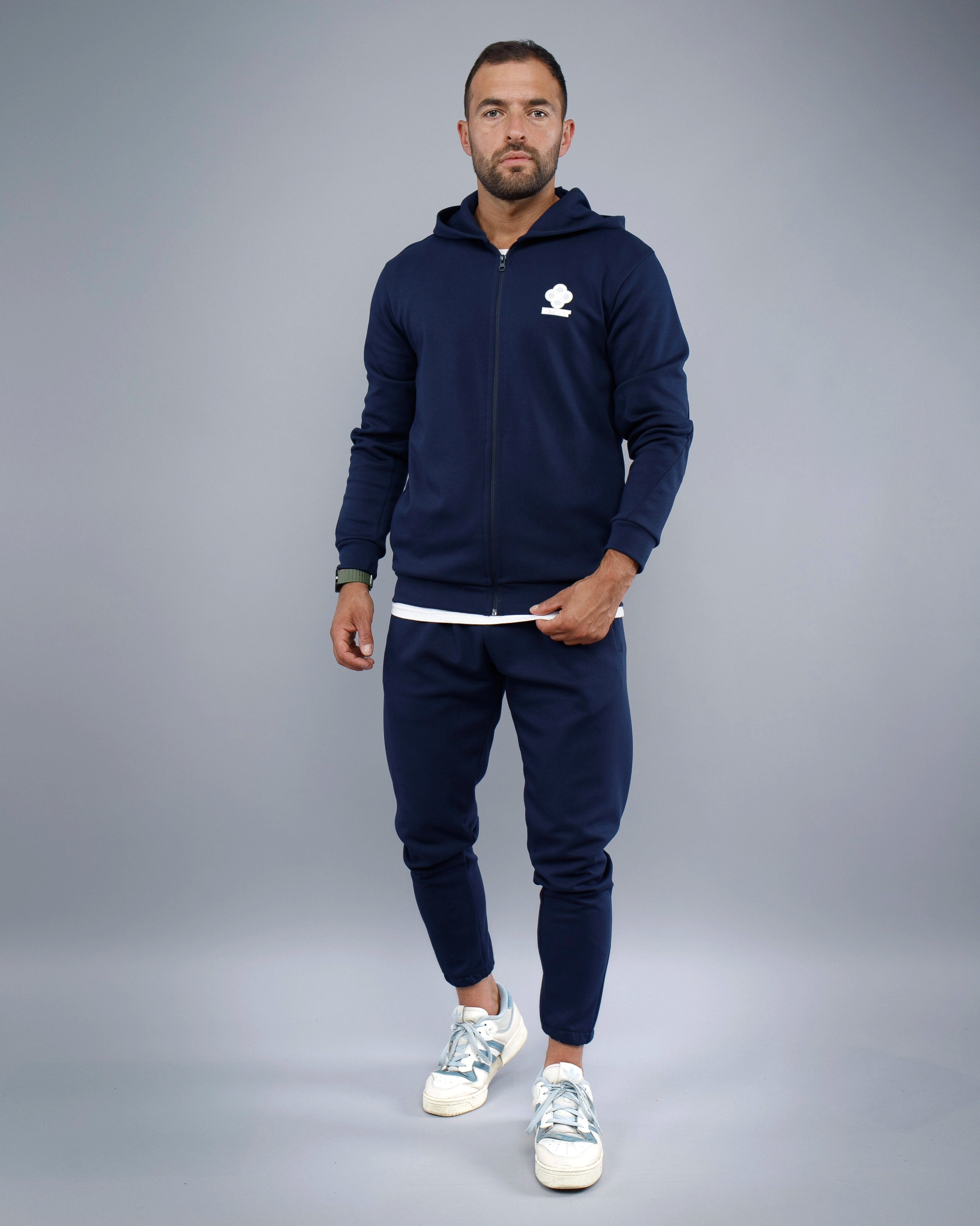 Man wearing a navy blue tracksuit with a logo on a gray background