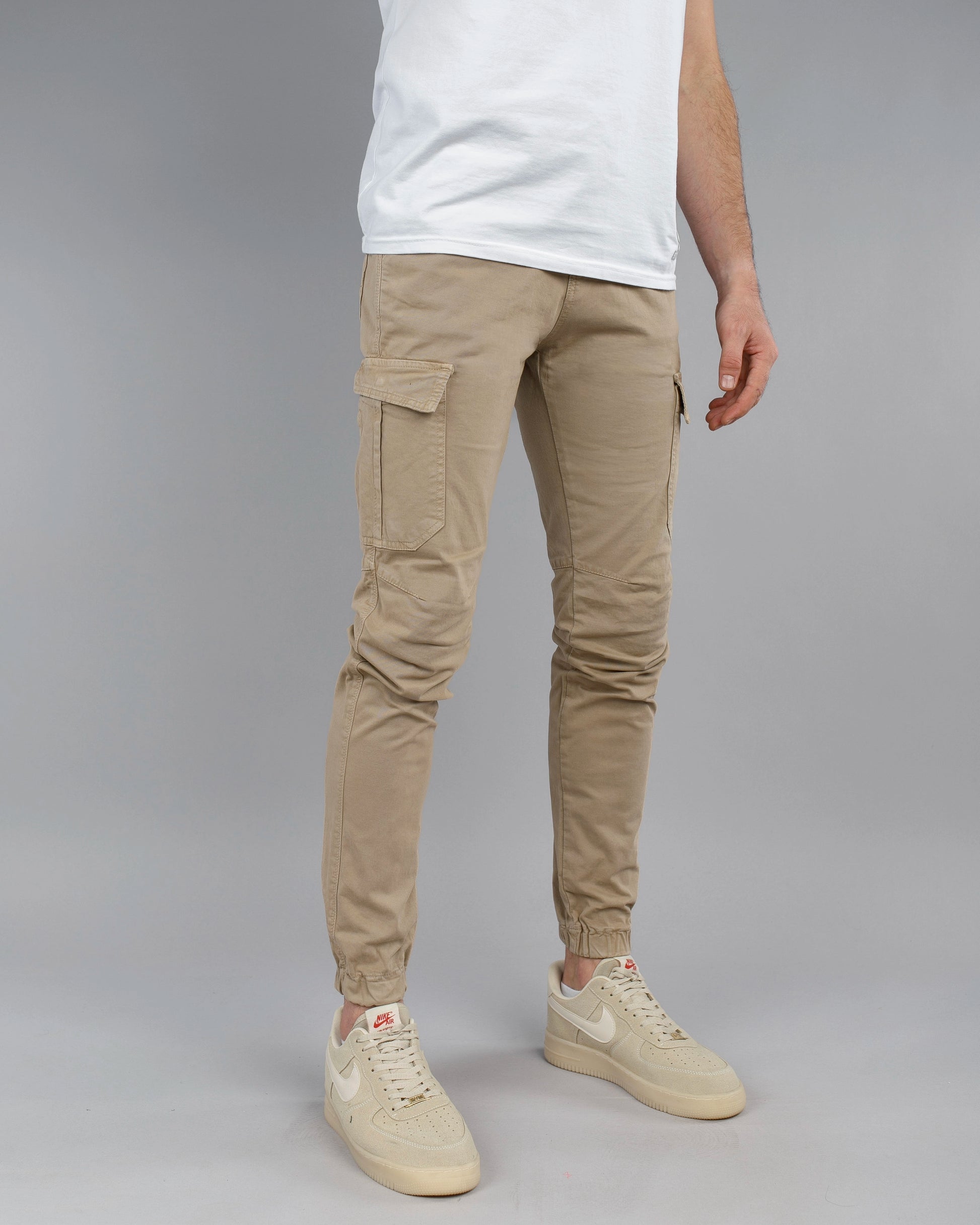 Person wearing beige cargo jogger pants and white sneakers on a gray background