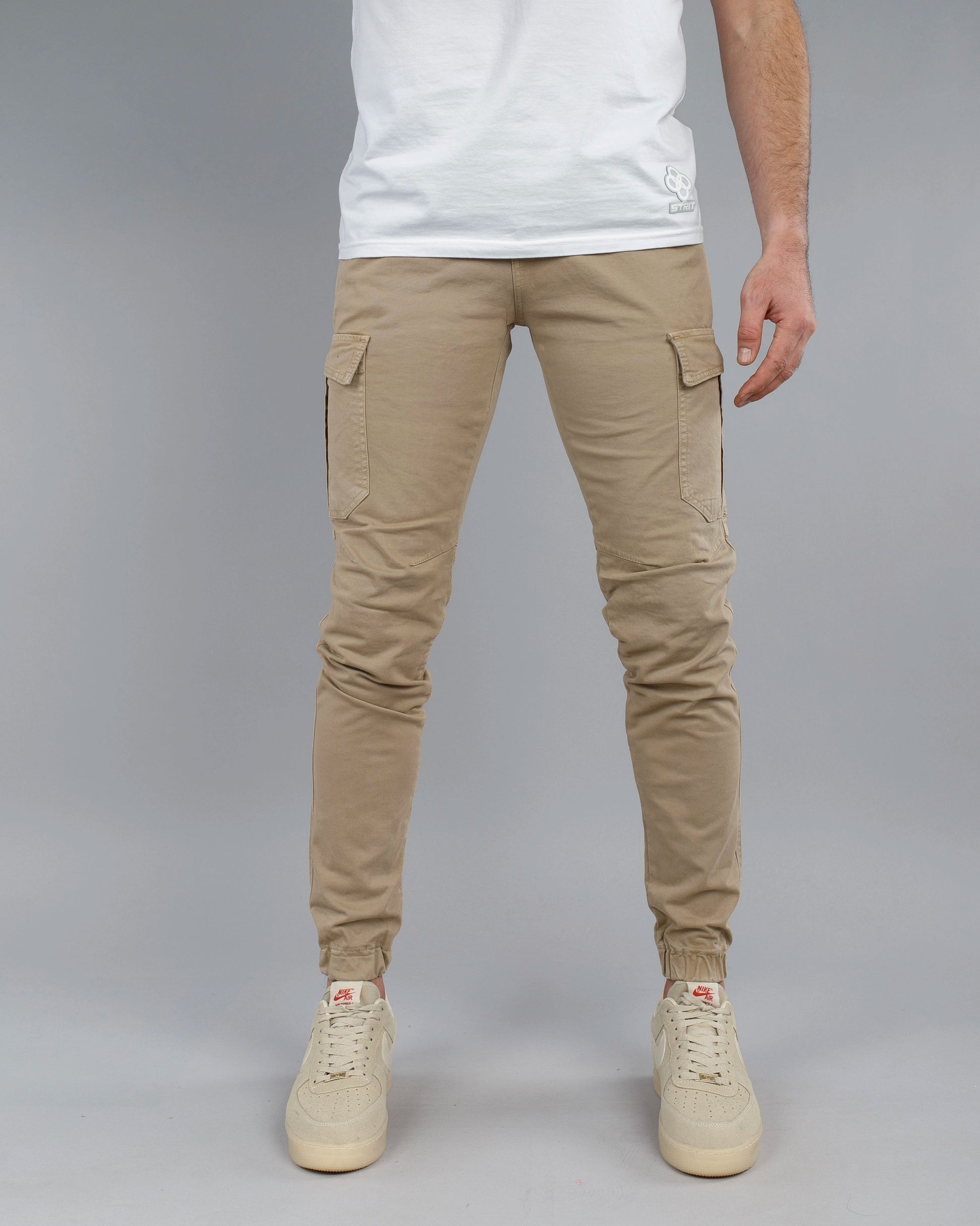 Person wearing beige cargo jogger pants and white sneakers on a gray background