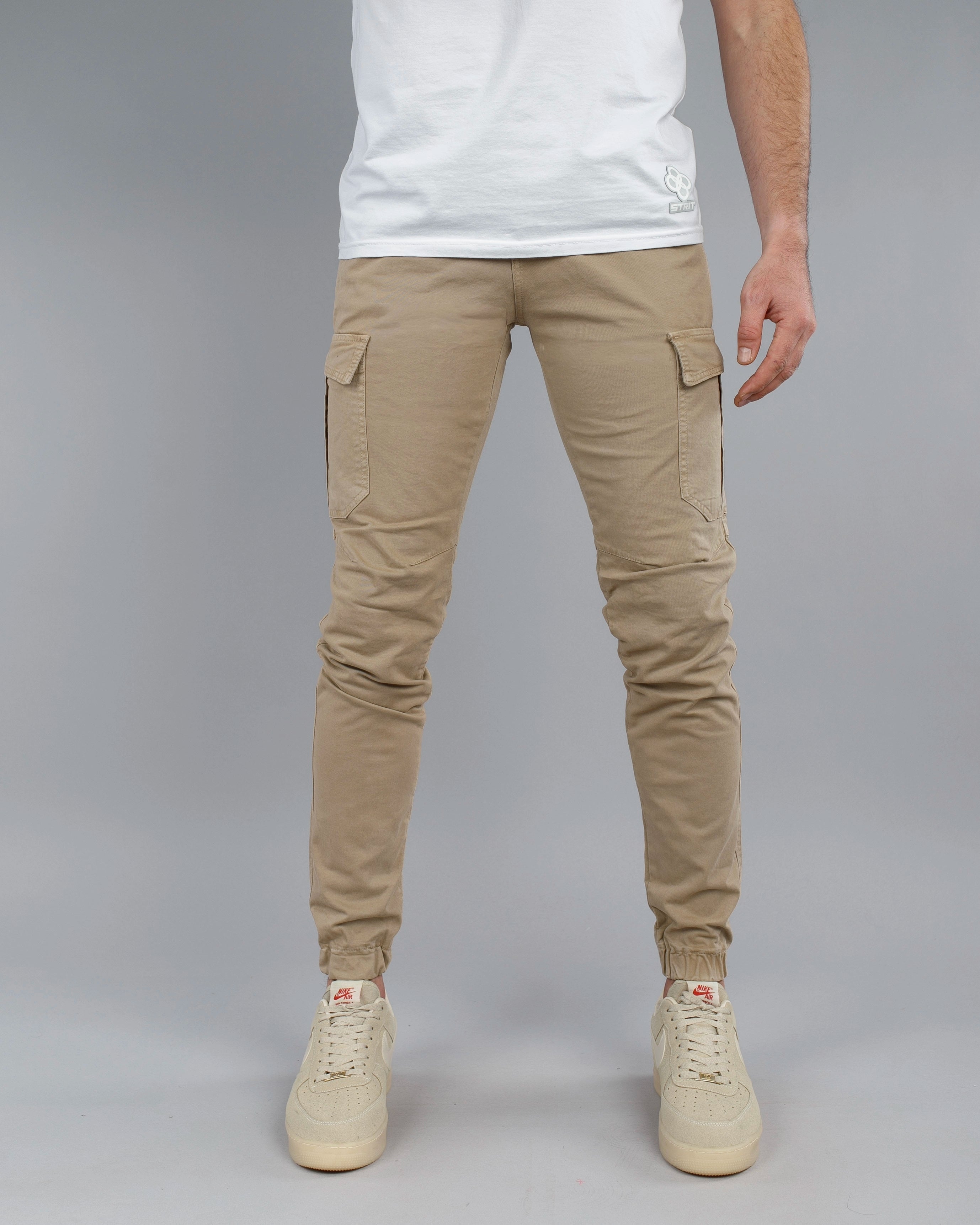 Person wearing beige cargo jogger pants and white sneakers on a gray background