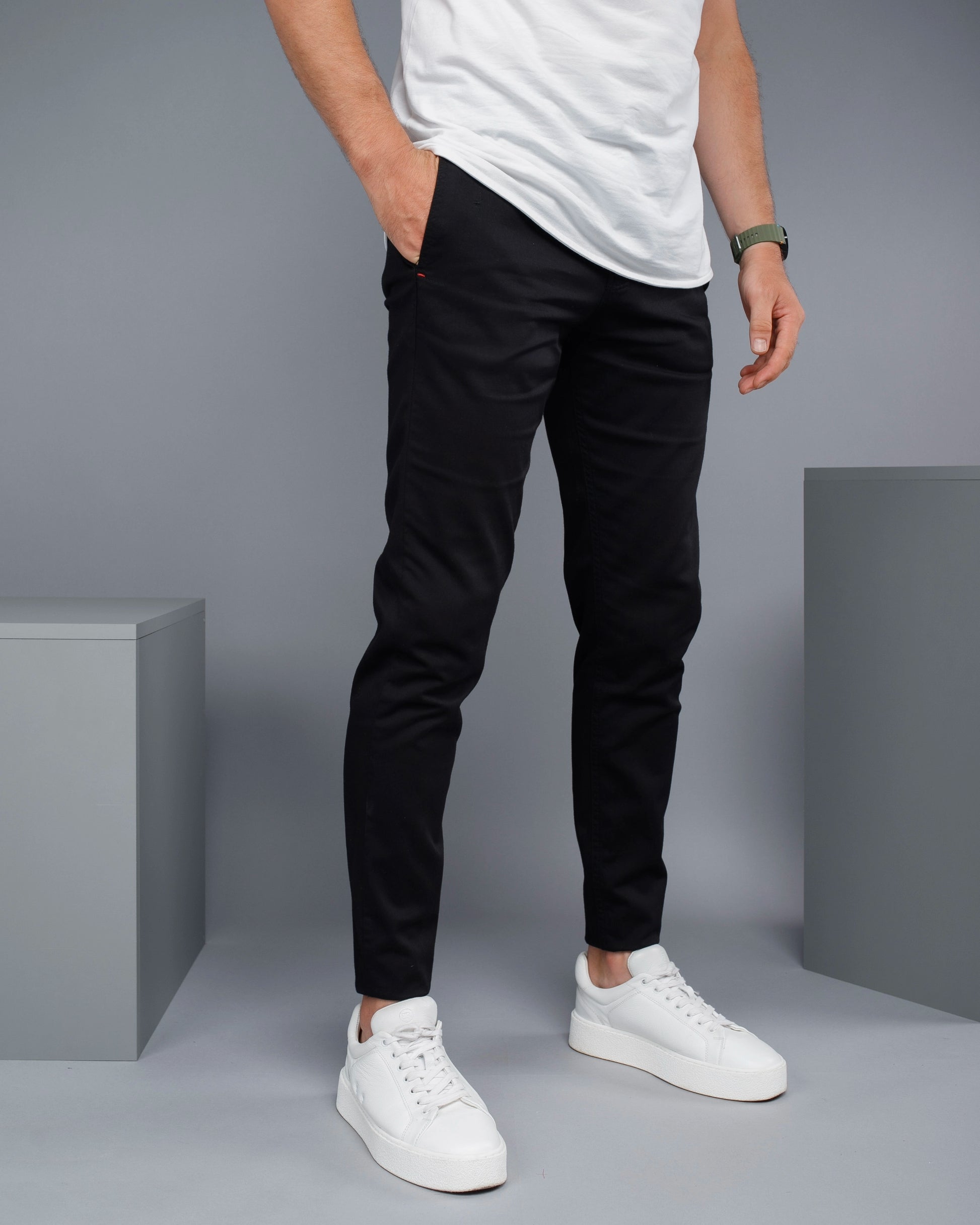 Person wearing black pants and white sneakers on a gray background