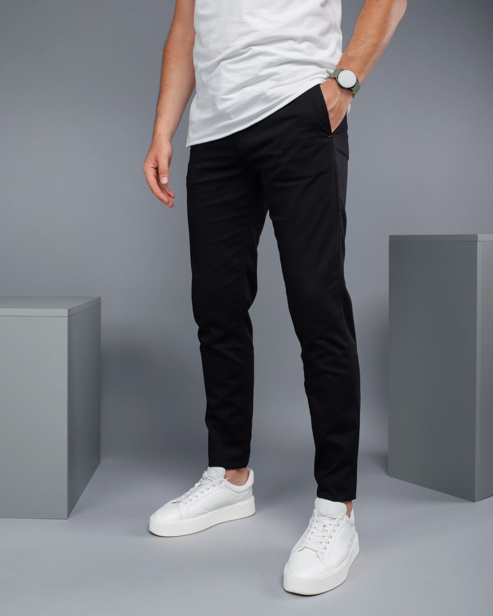 Person wearing black pants and white sneakers on a gray background