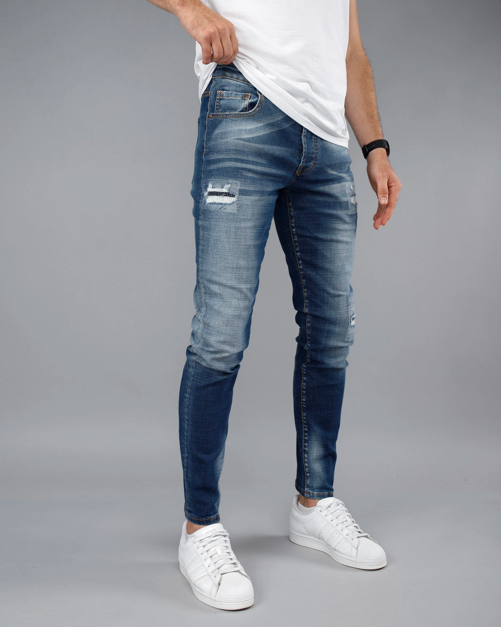 Person wearing blue distressed jeans and white sneakers on a gray background