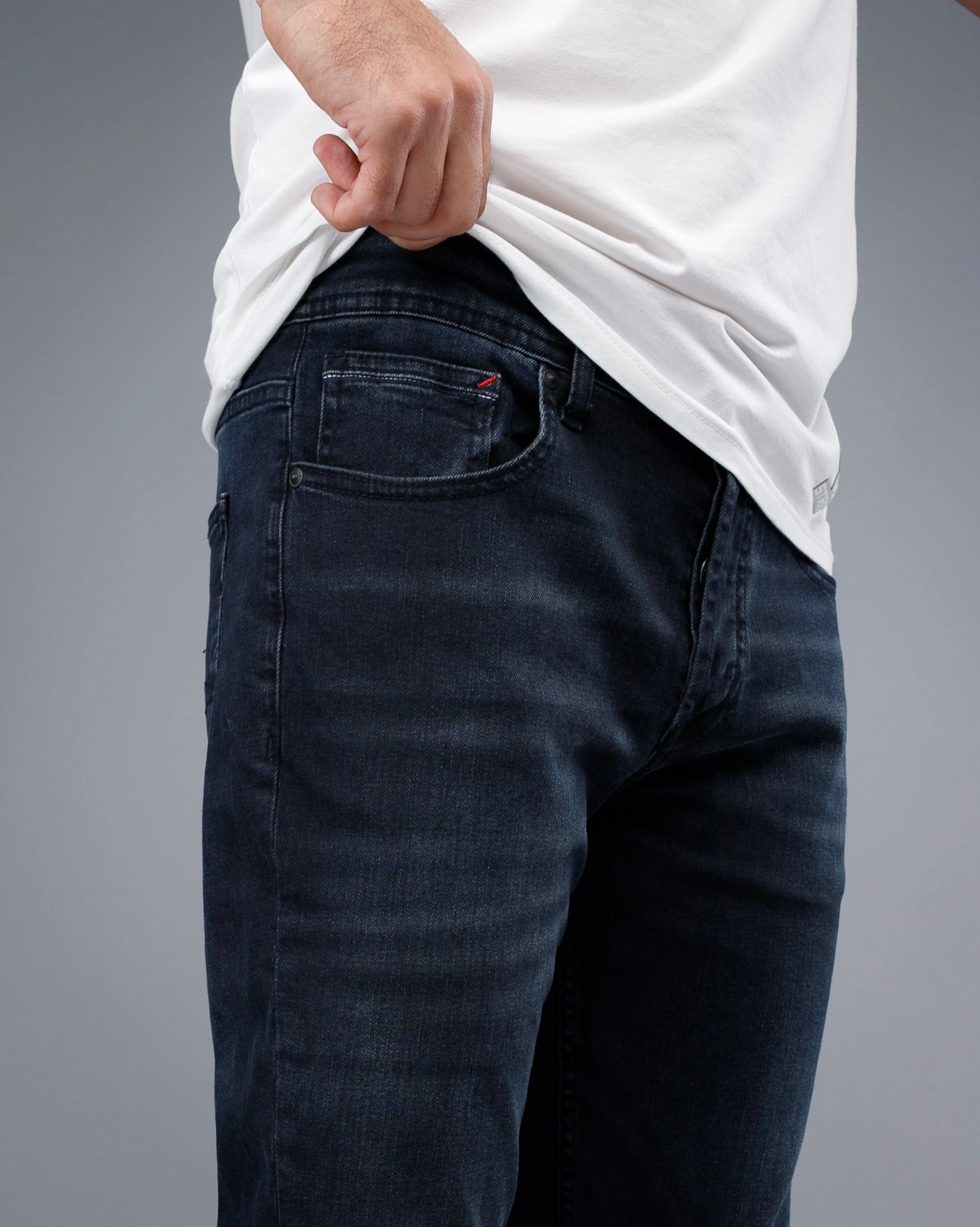 Person wearing dark jeans and a white shirt on a gray background