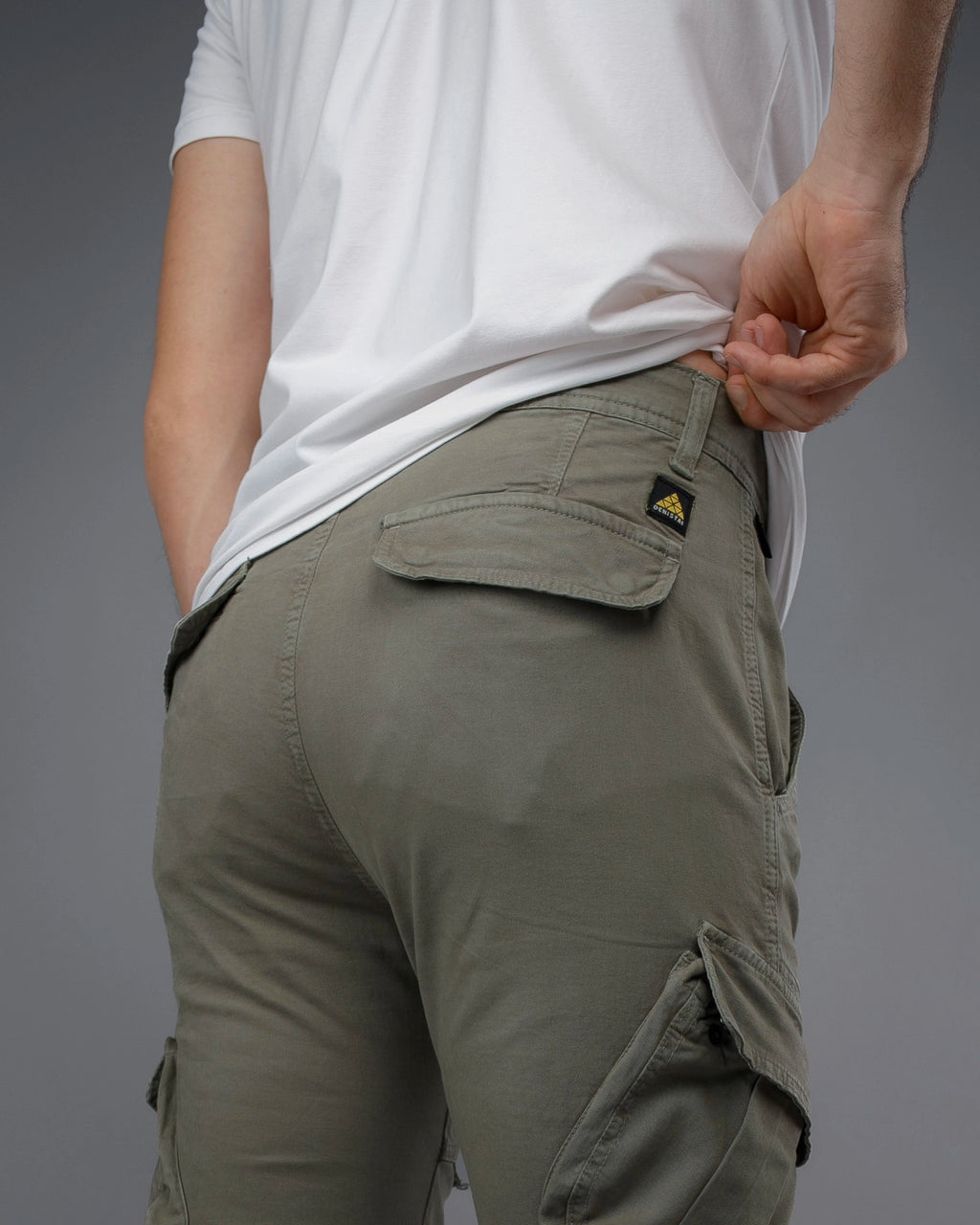 Person wearing olive green cargo pants with a visible brand logo on a gray background