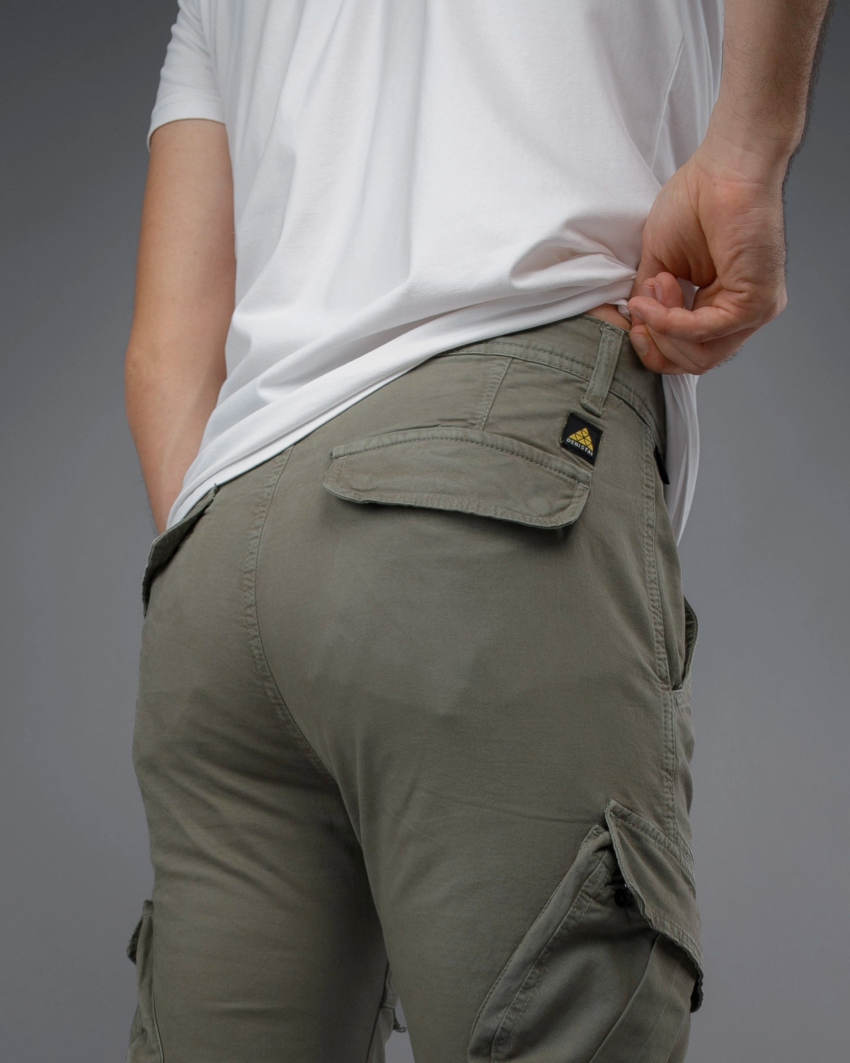Person wearing olive green cargo pants with a visible brand logo on a gray background