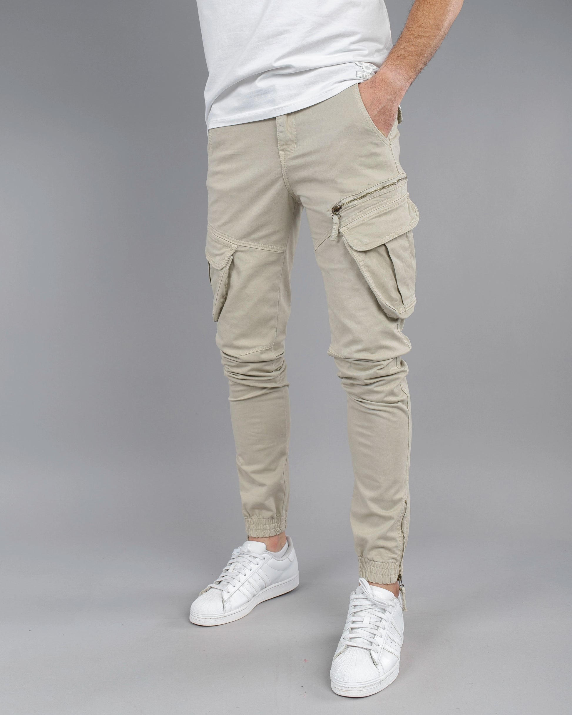 Person wearing beige cargo pants and white sneakers on a gray background