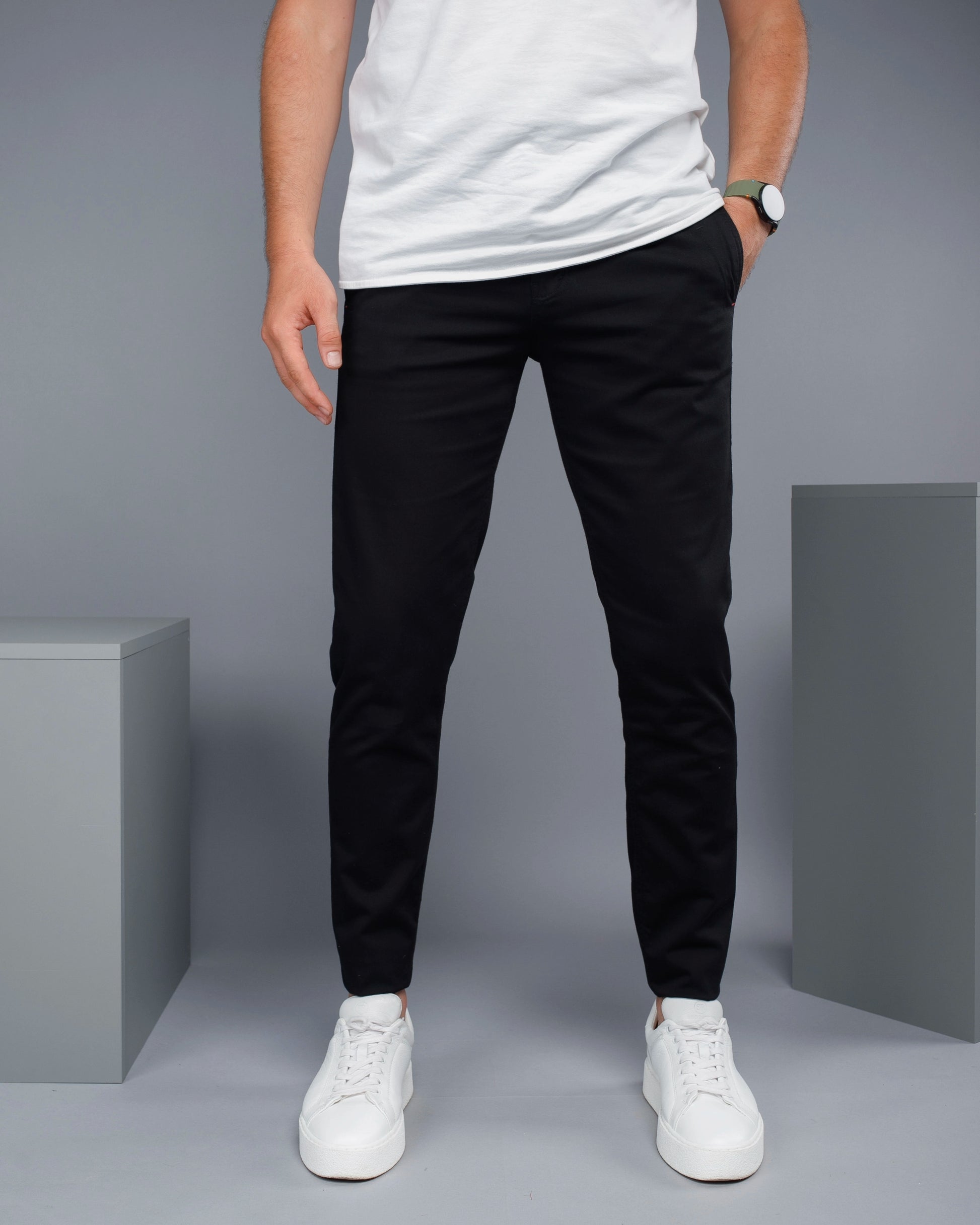 Person wearing black pants and white sneakers on a gray background