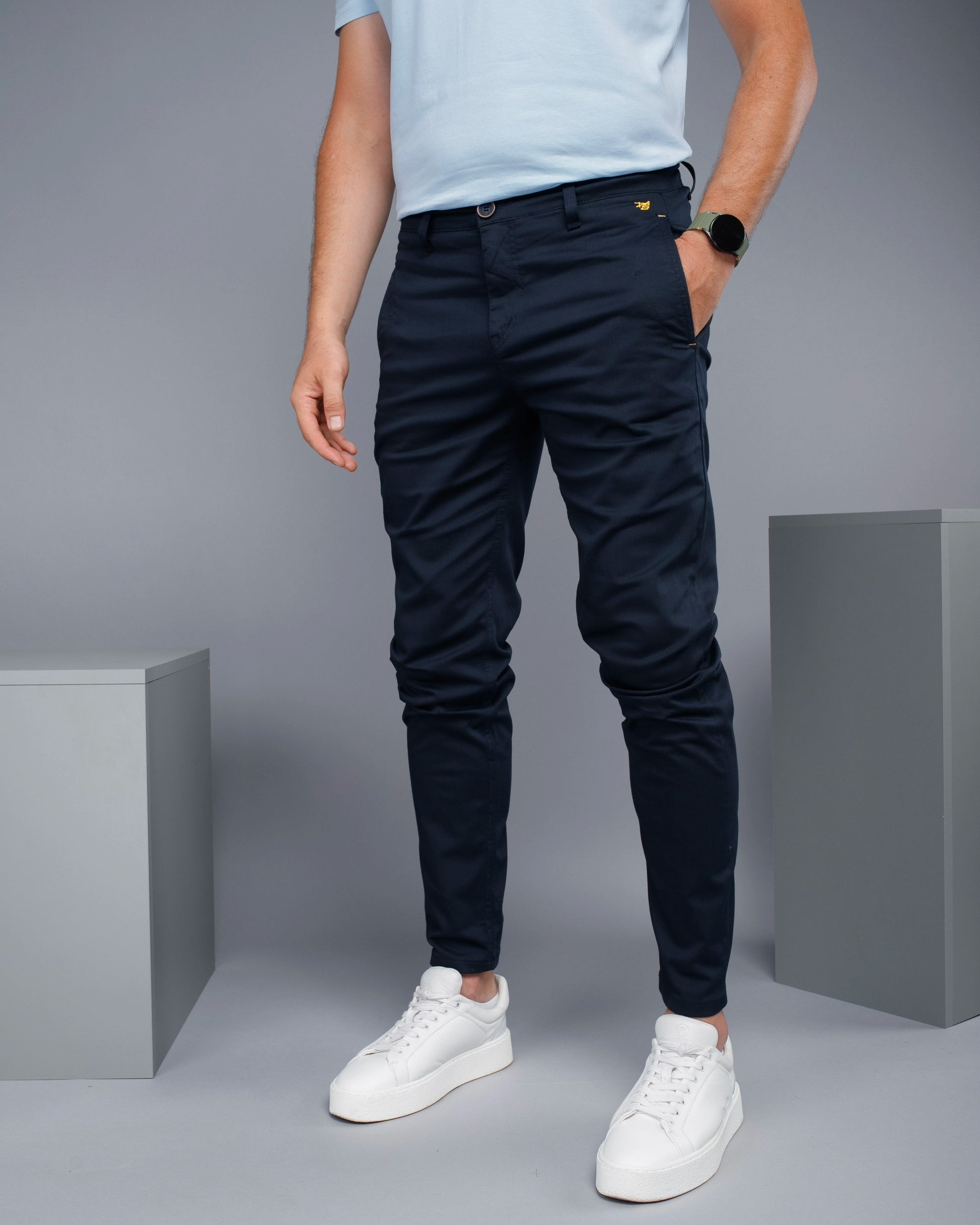 Person wearing navy pants and white sneakers on a gray background