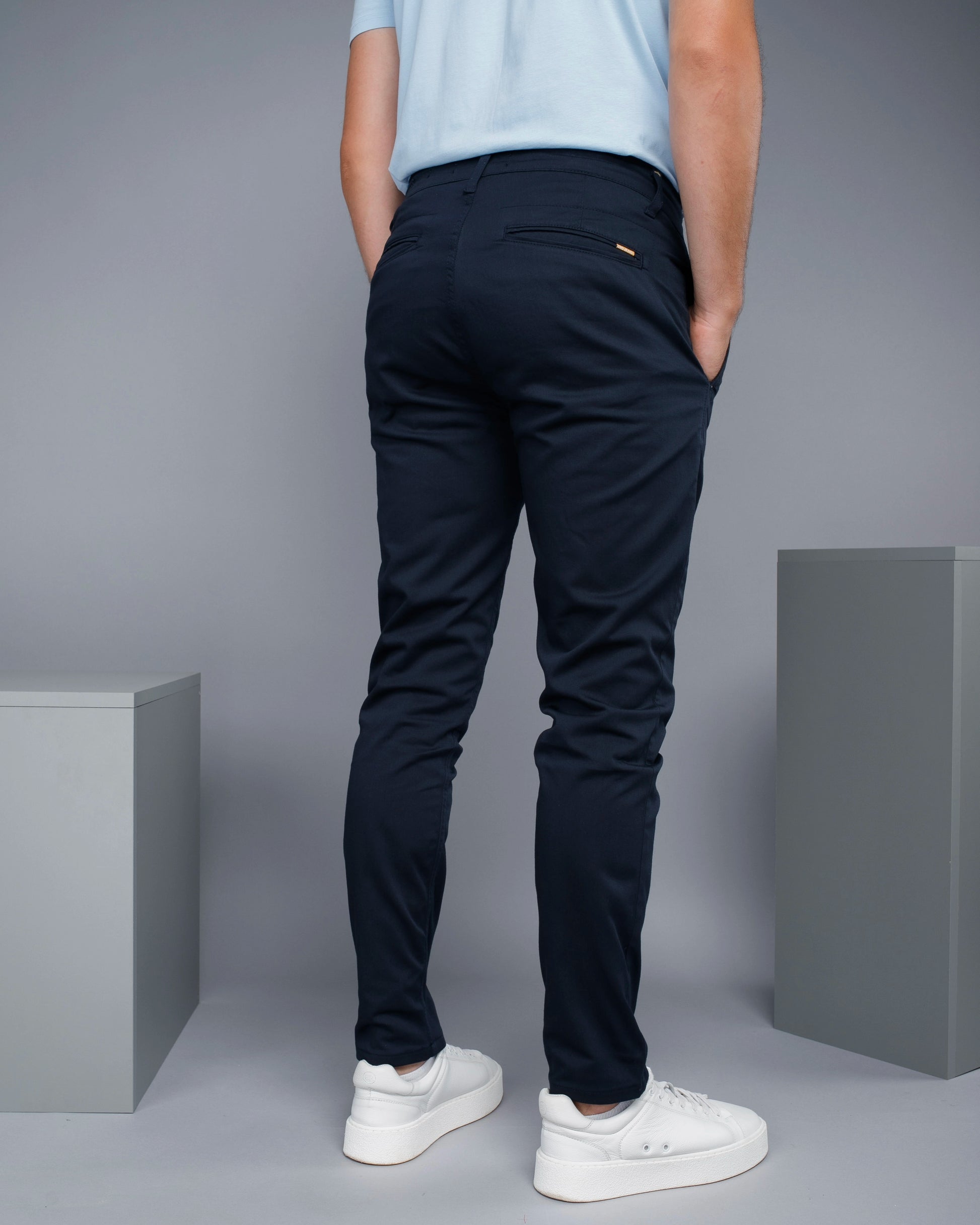 Person wearing navy pants and white sneakers against a gray background