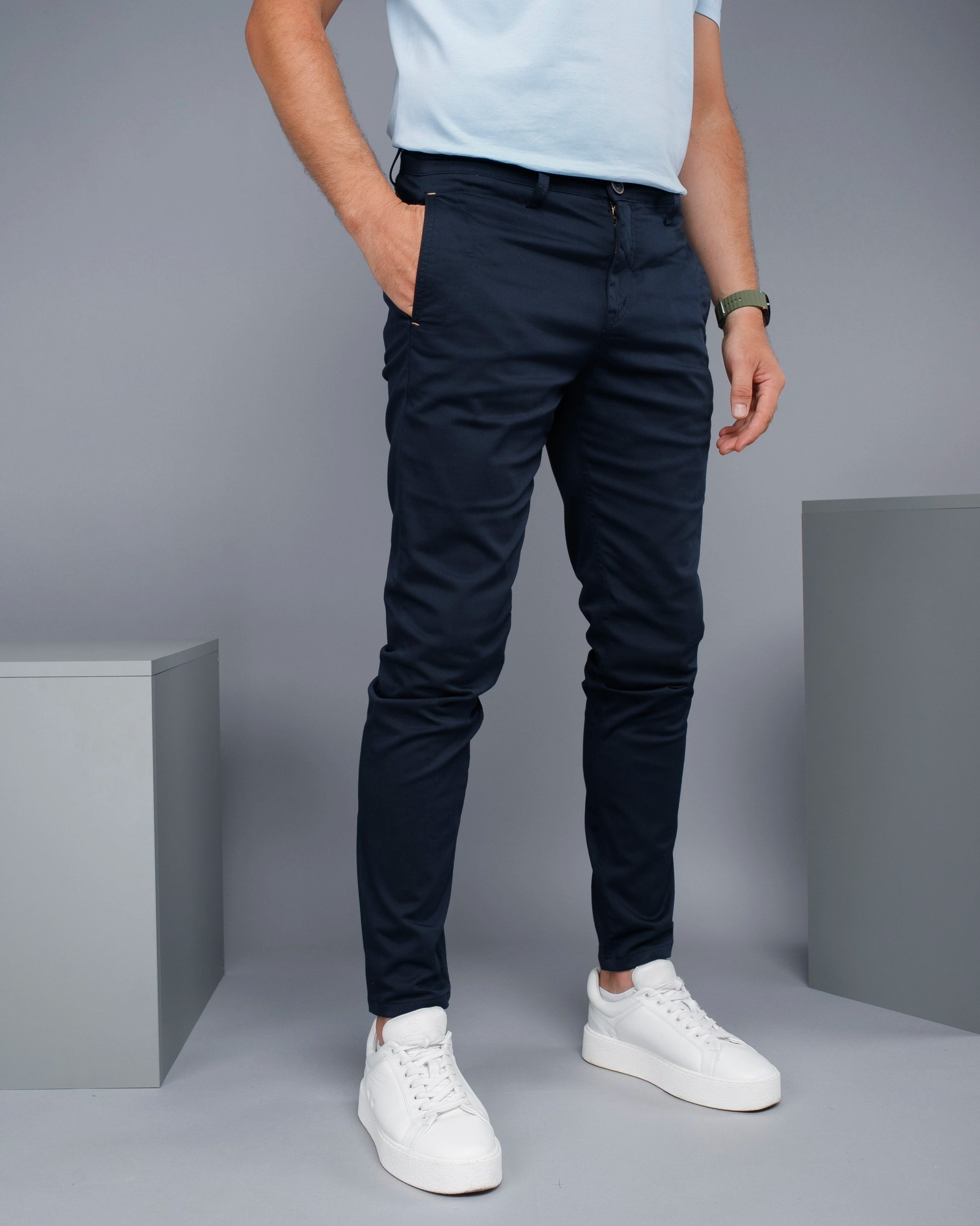 Person wearing navy pants and white sneakers on a gray background