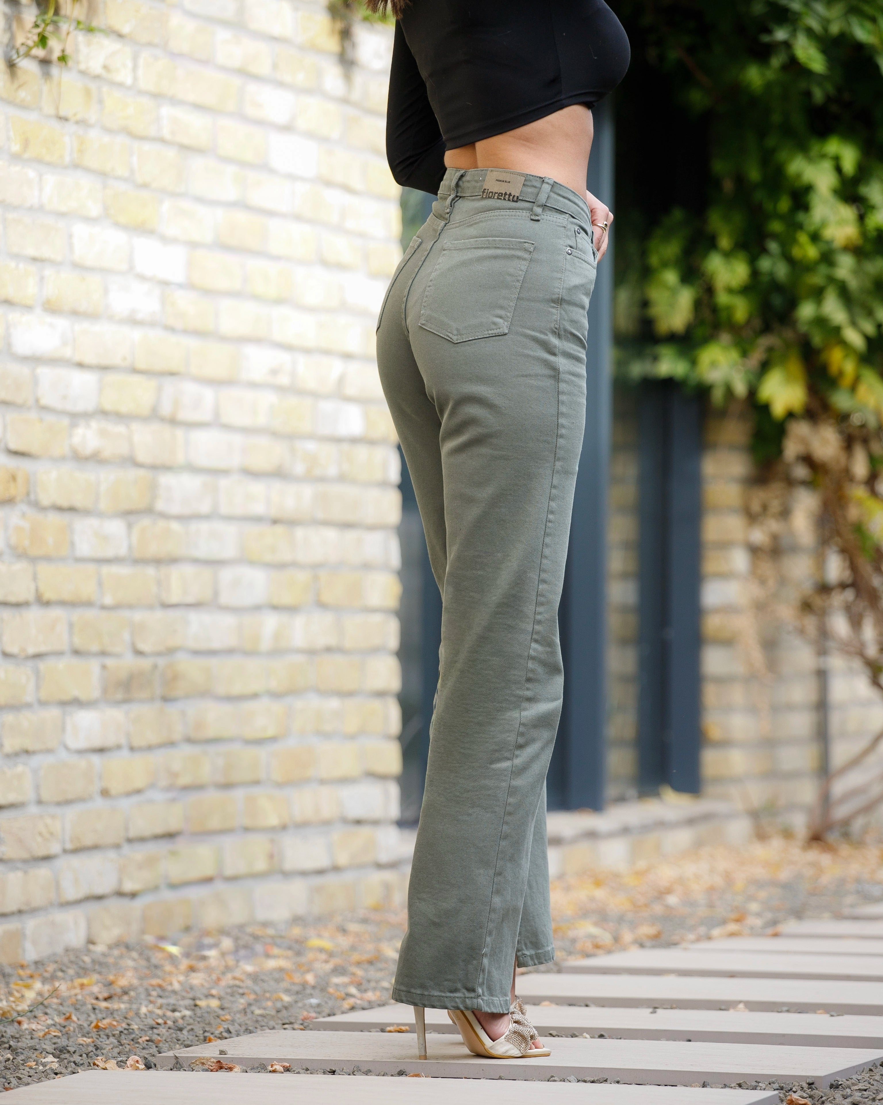 Person wearing green flared jeans standing against a brick wall.