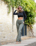 Woman wearing a black long-sleeve top and green high-waisted pants standing outdoors.