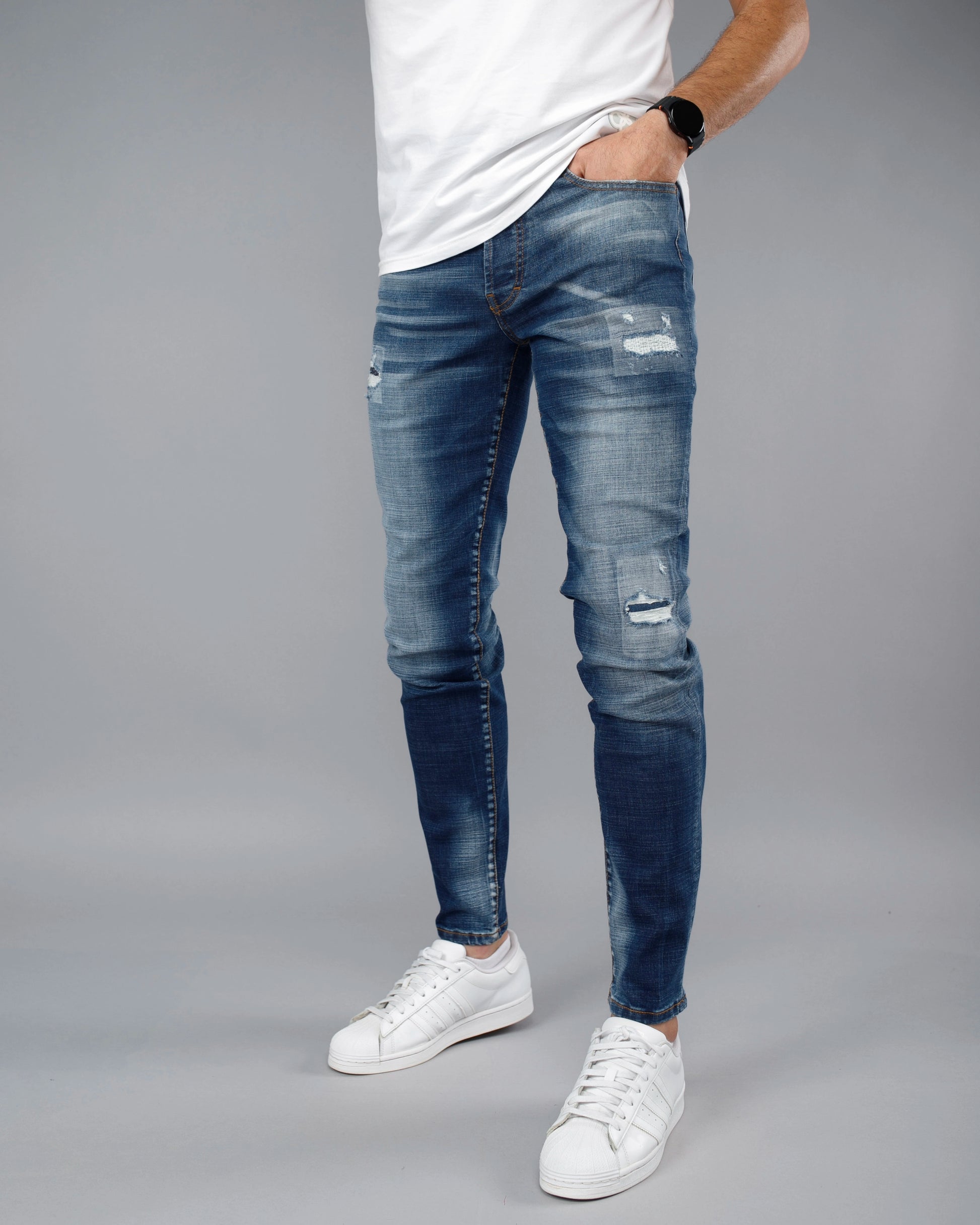 Person wearing blue ripped jeans and white sneakers on a gray background