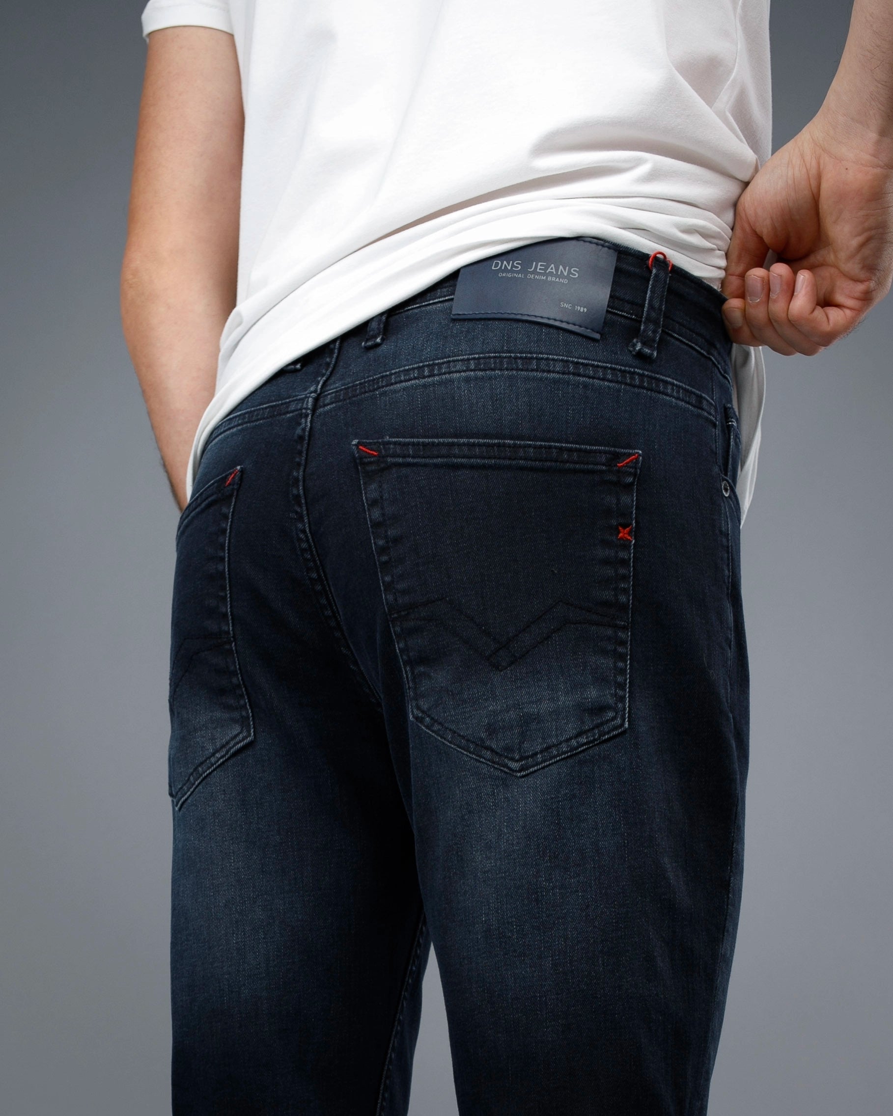 Person wearing dark blue jeans with a visible brand label on a gray background