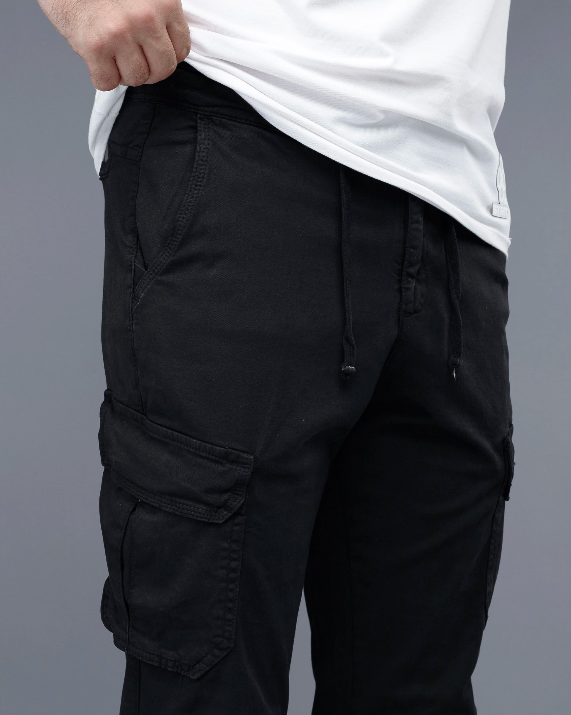 Black cargo pants worn with a white shirt on a gray background