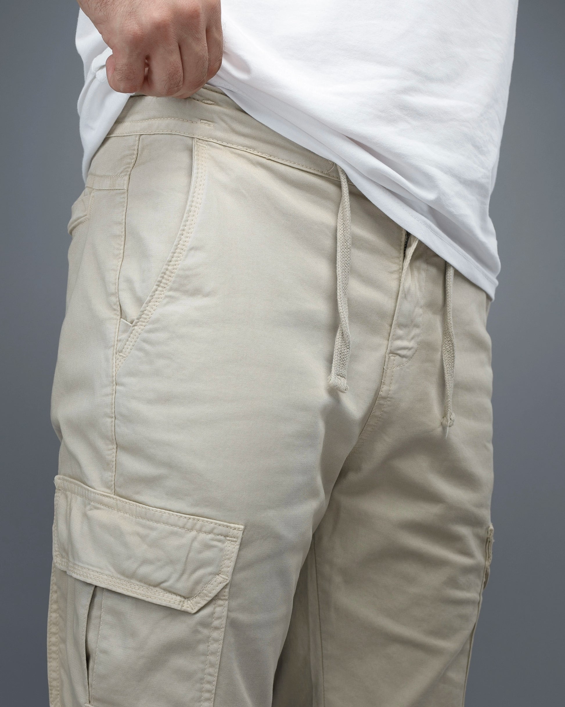 Beige cargo pants worn with a white shirt on a gray background