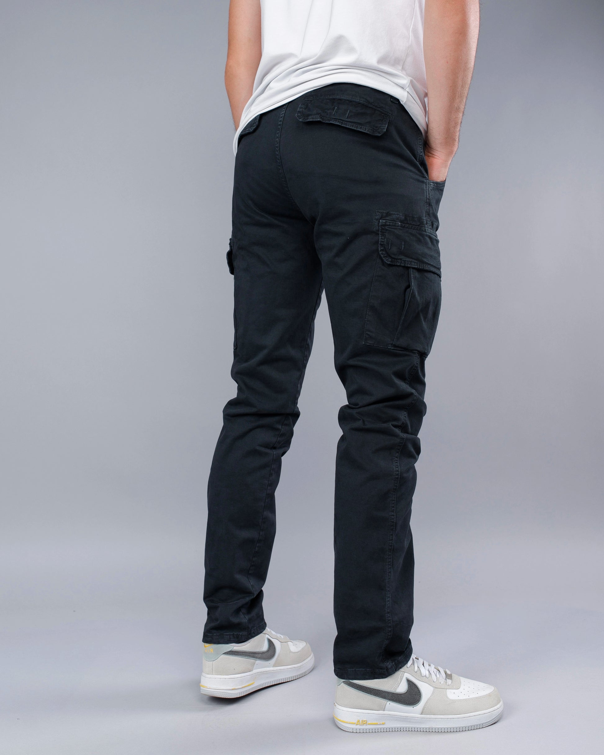 Person wearing black cargo pants and white sneakers on a gray background