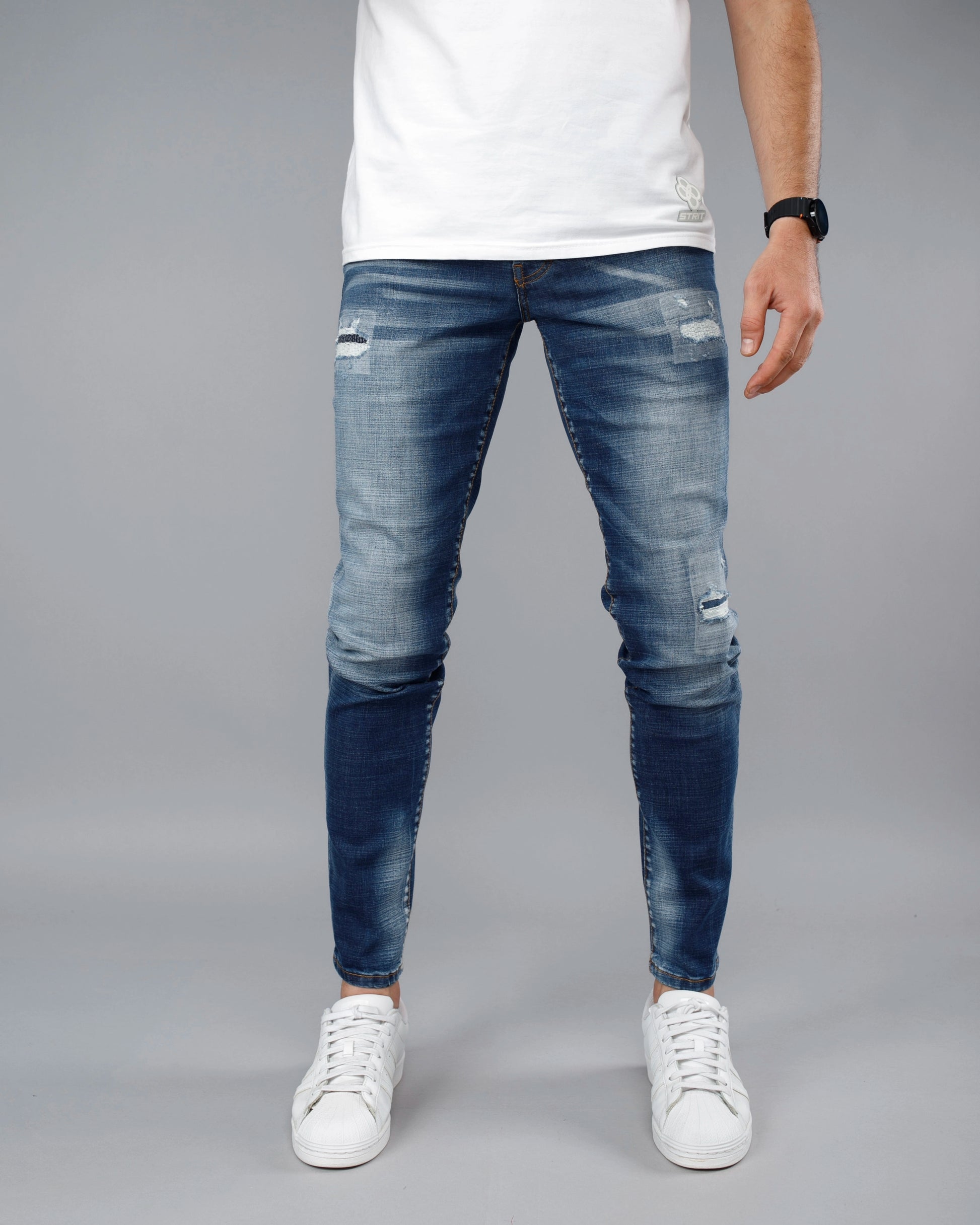Person wearing blue distressed jeans and white sneakers on a gray background