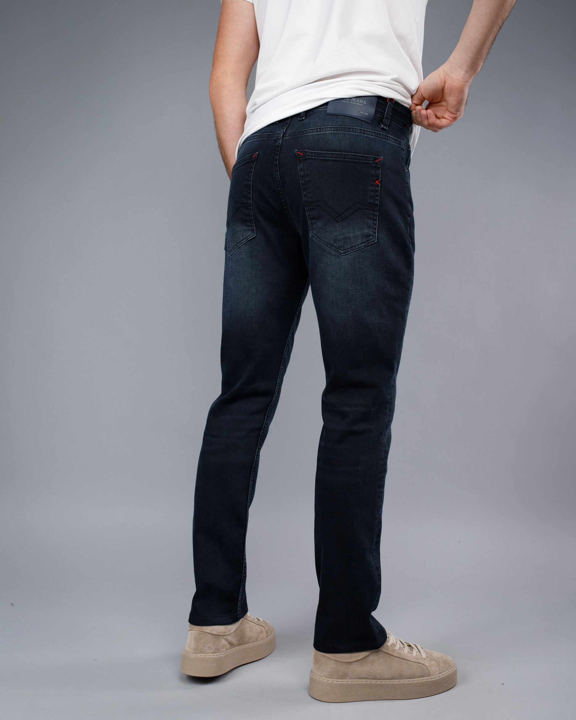 Person wearing dark jeans and a white shirt on a gray background