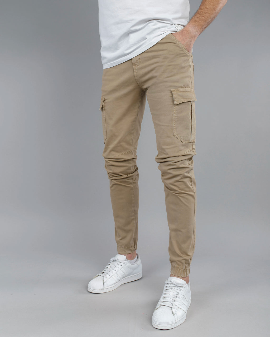 Person wearing beige cargo pants and white sneakers on a gray background