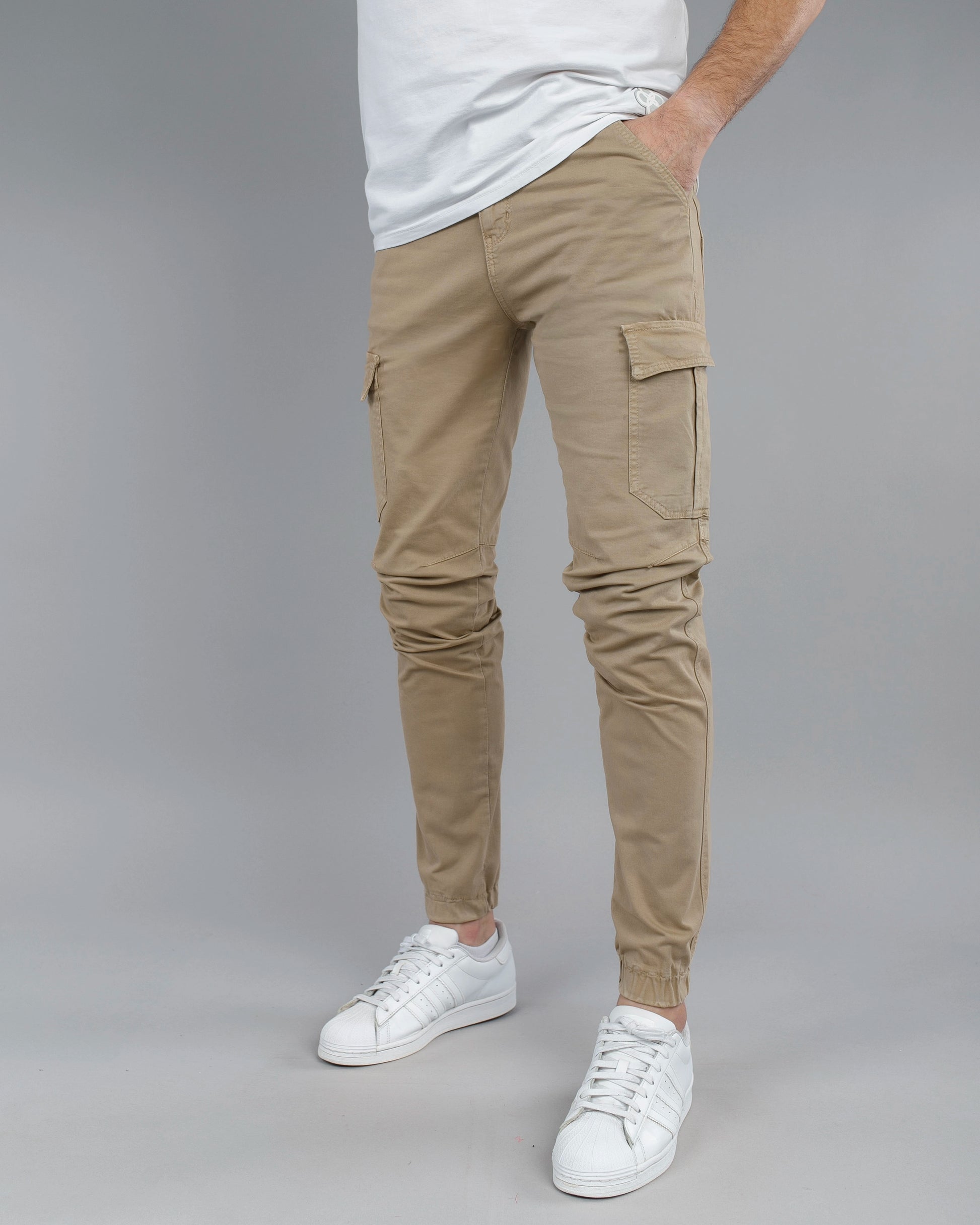 Person wearing beige cargo pants and white sneakers on a gray background