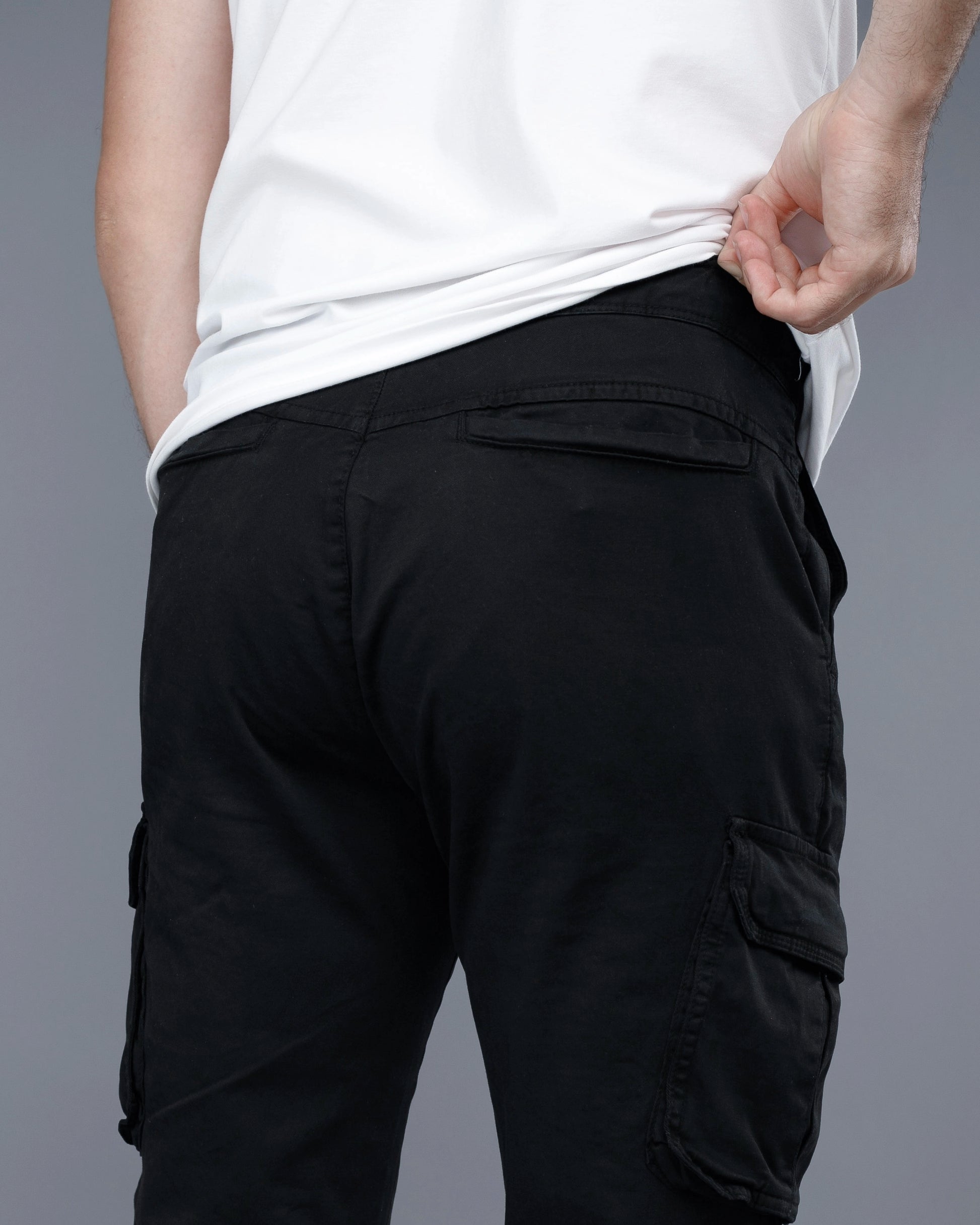 Person wearing black cargo pants and a white shirt on a gray background