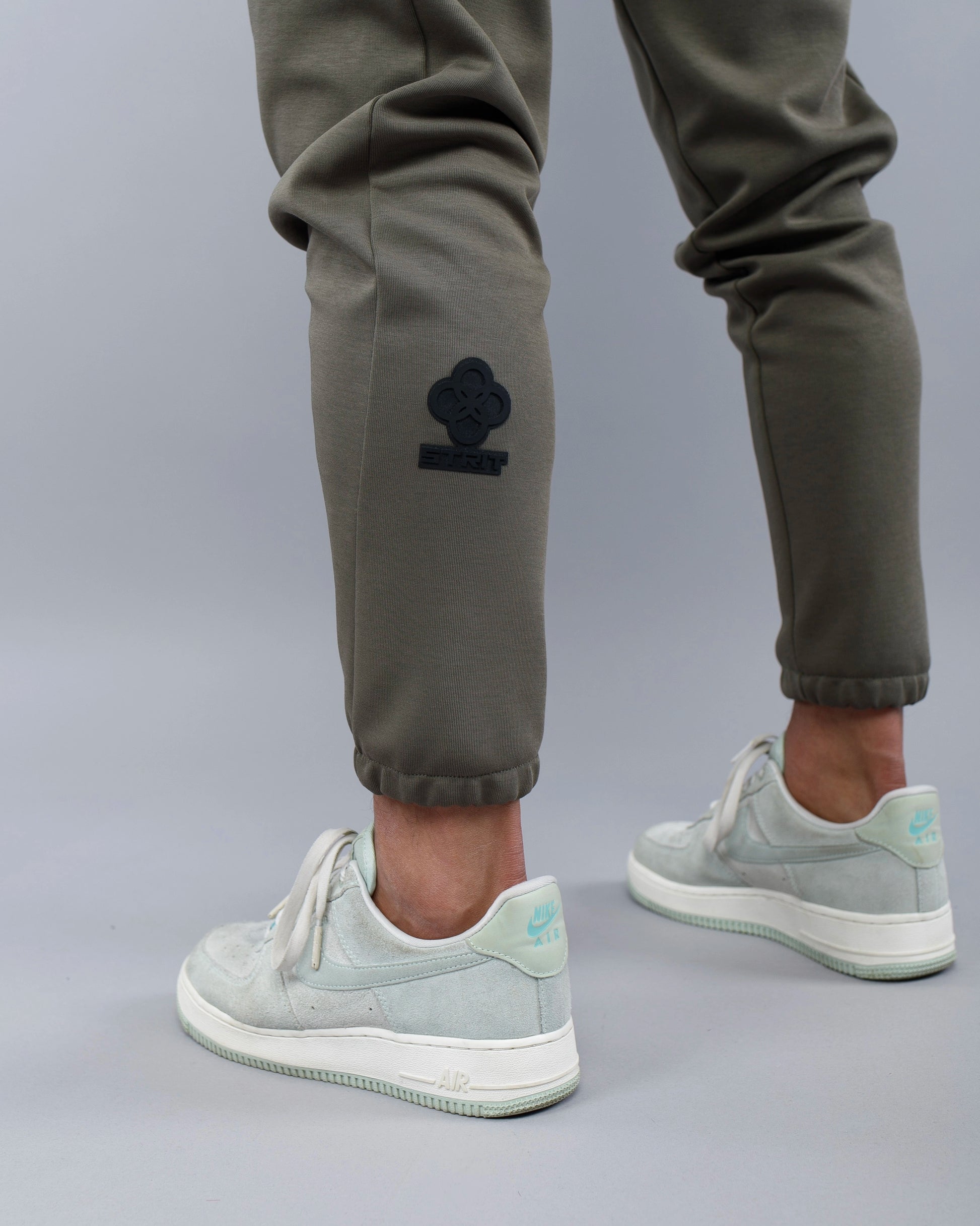 Person wearing green pants with a logo and light gray sneakers on a gray background