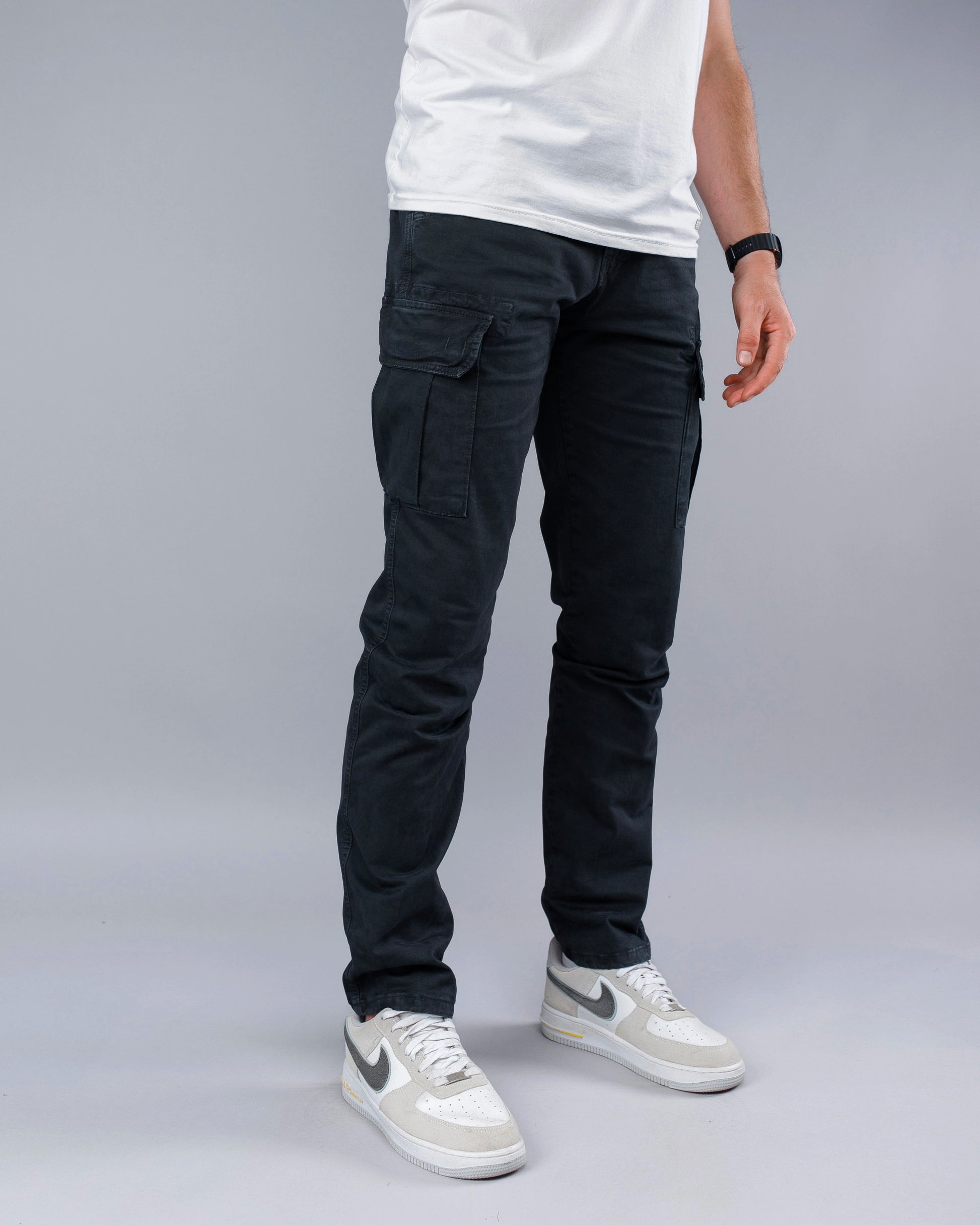 Person wearing black cargo pants and white sneakers on a gray background