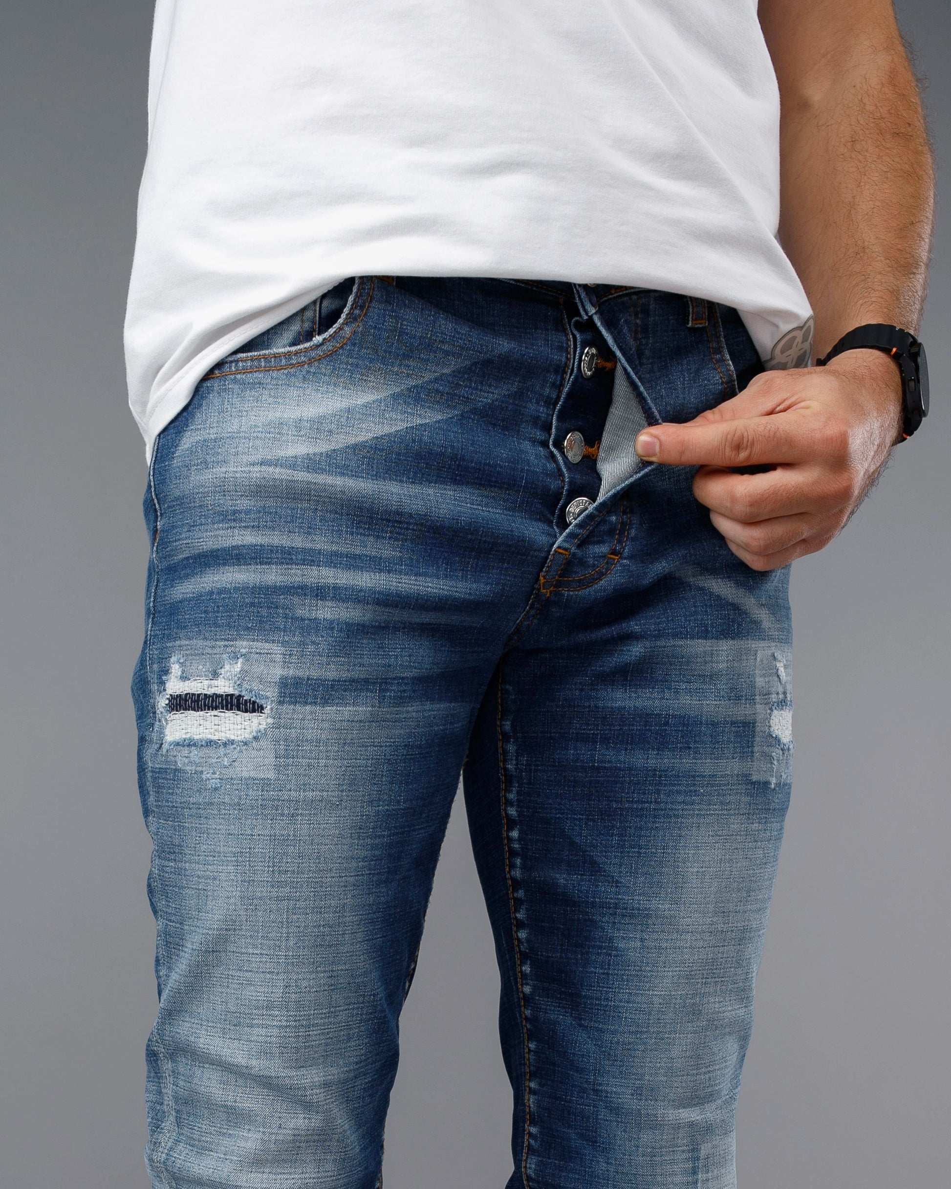Person wearing blue distressed jeans and a white shirt on a gray background