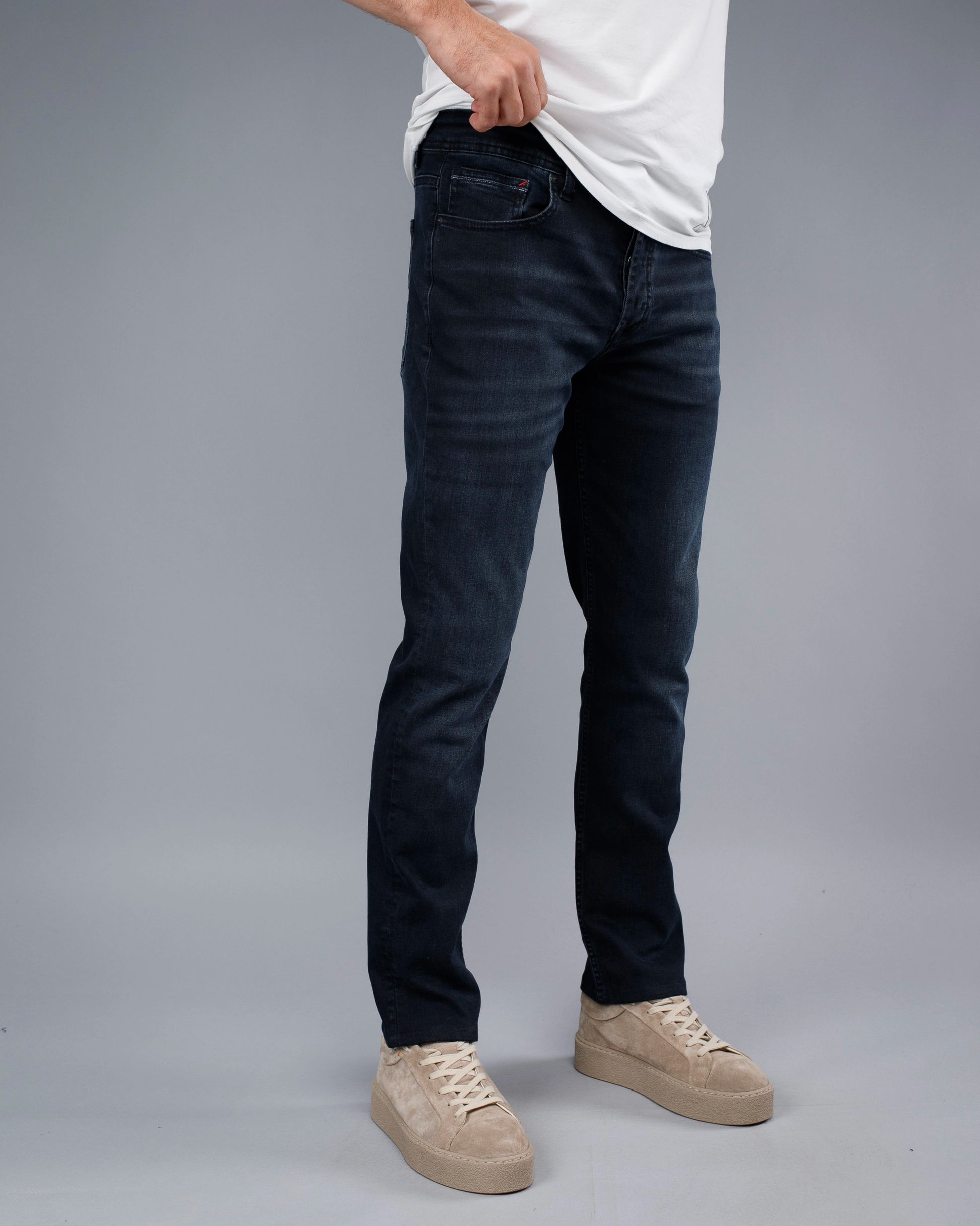 Person wearing dark jeans and beige sneakers on a gray background
