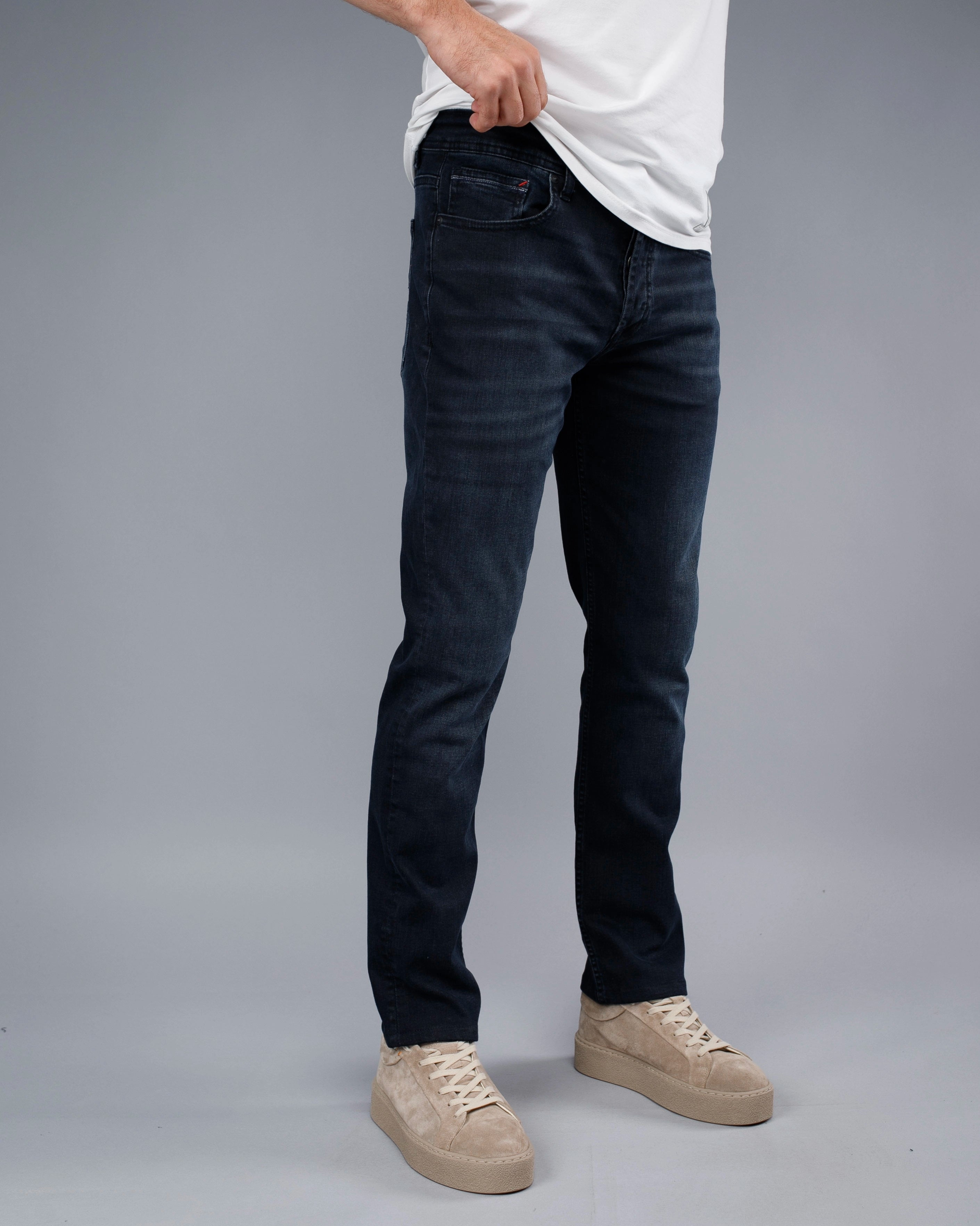 Person wearing dark jeans and beige sneakers on a gray background