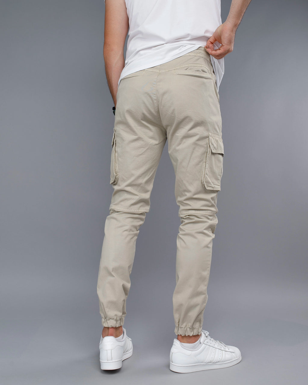 Person wearing beige cargo jogger pants and white sneakers on a gray background