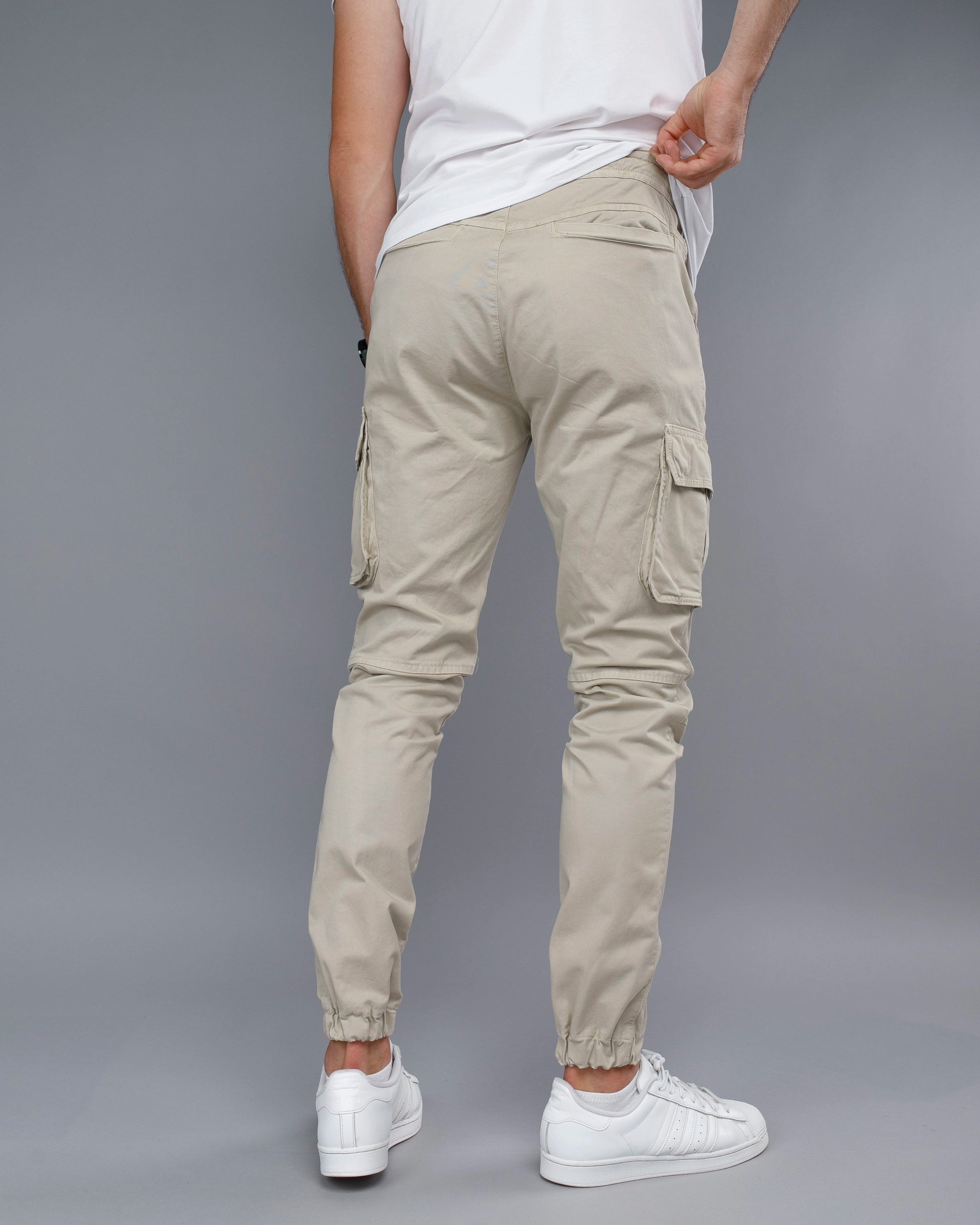 Person wearing beige cargo jogger pants and white sneakers on a gray background