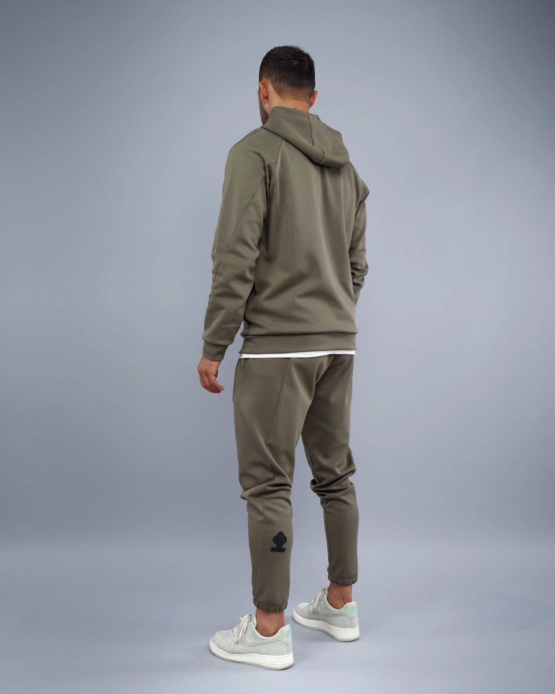 Person wearing a green tracksuit with a hood on a gray background