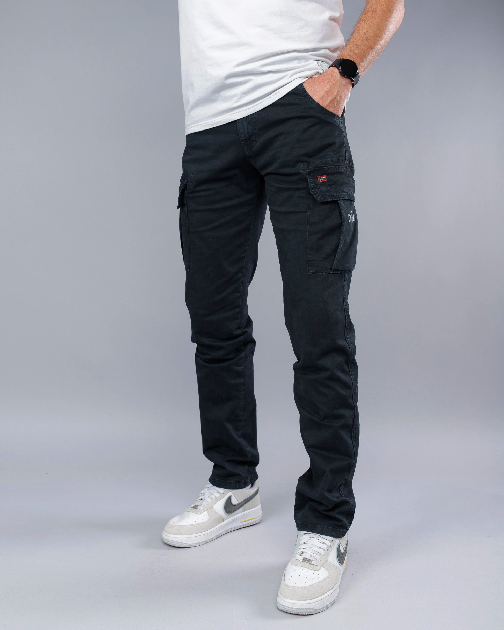 Person wearing black cargo pants and white sneakers on a gray background