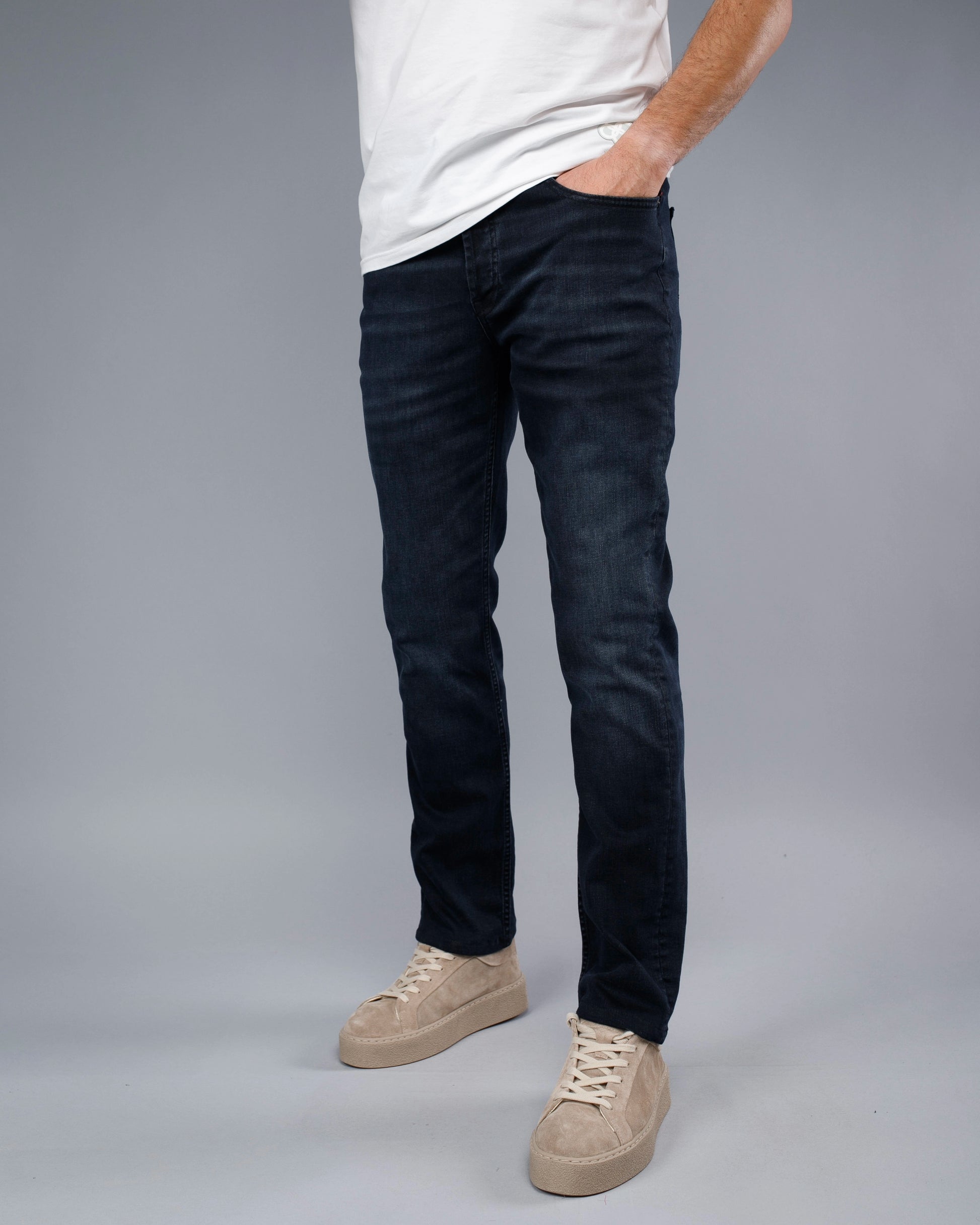 Person wearing dark jeans and beige sneakers on a gray background